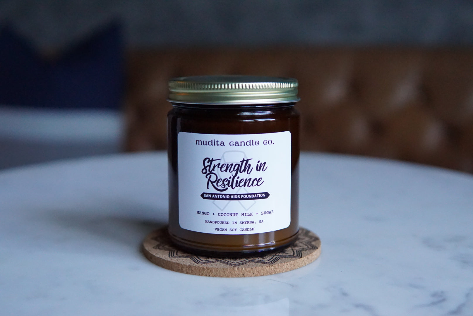 Strength in Resilience candle in amber glass jar with gold lid, featuring tropical mango and coconut milk scent.