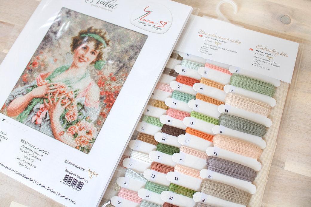 The Girl with Roses B553L Counted Cross-Stitch Kit featuring colorful threads, Aida canvas, and a needle.