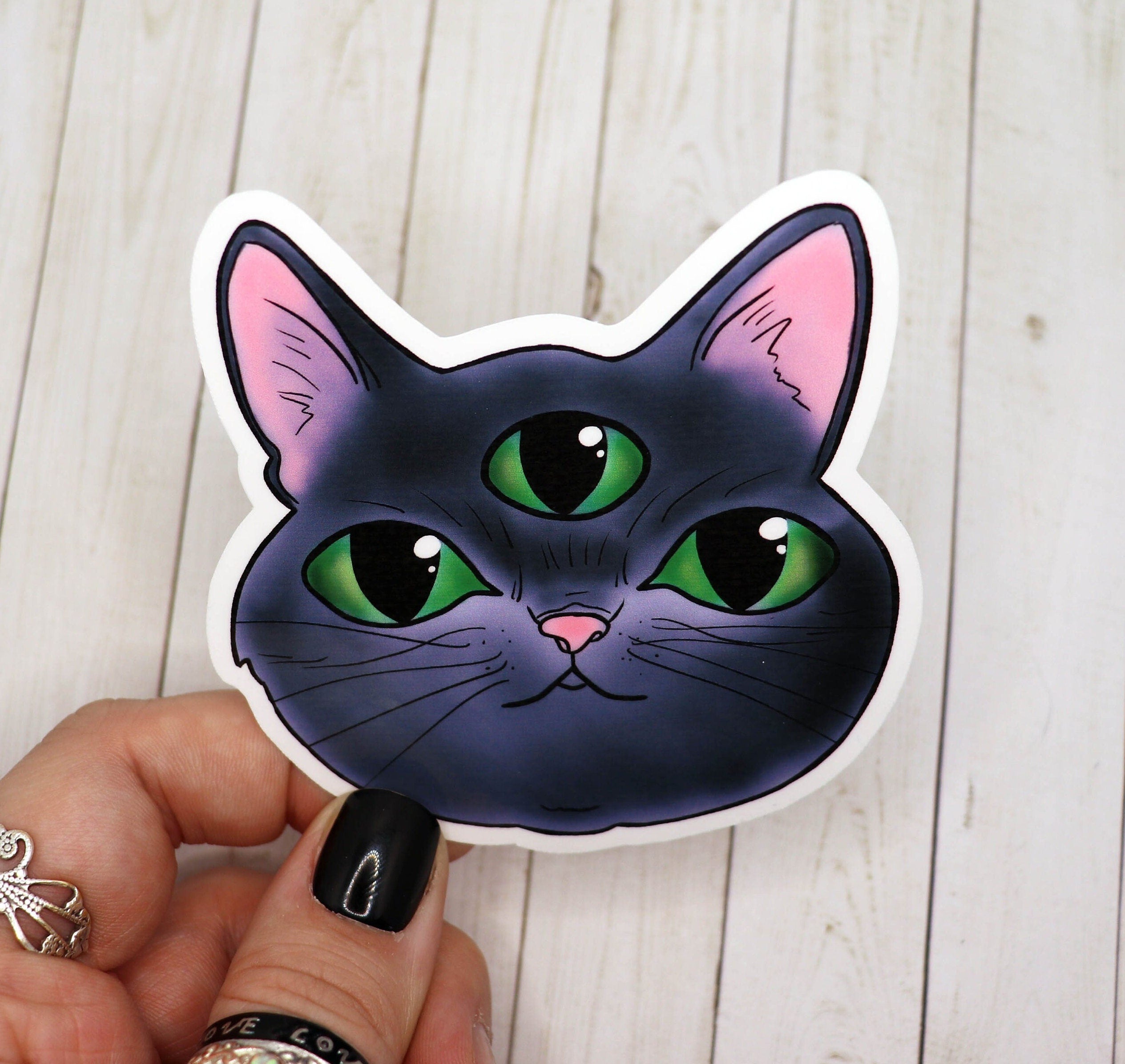 A vibrant three eyed cat sticker on a matte vinyl surface, showcasing a whimsical design perfect for personalizing items.