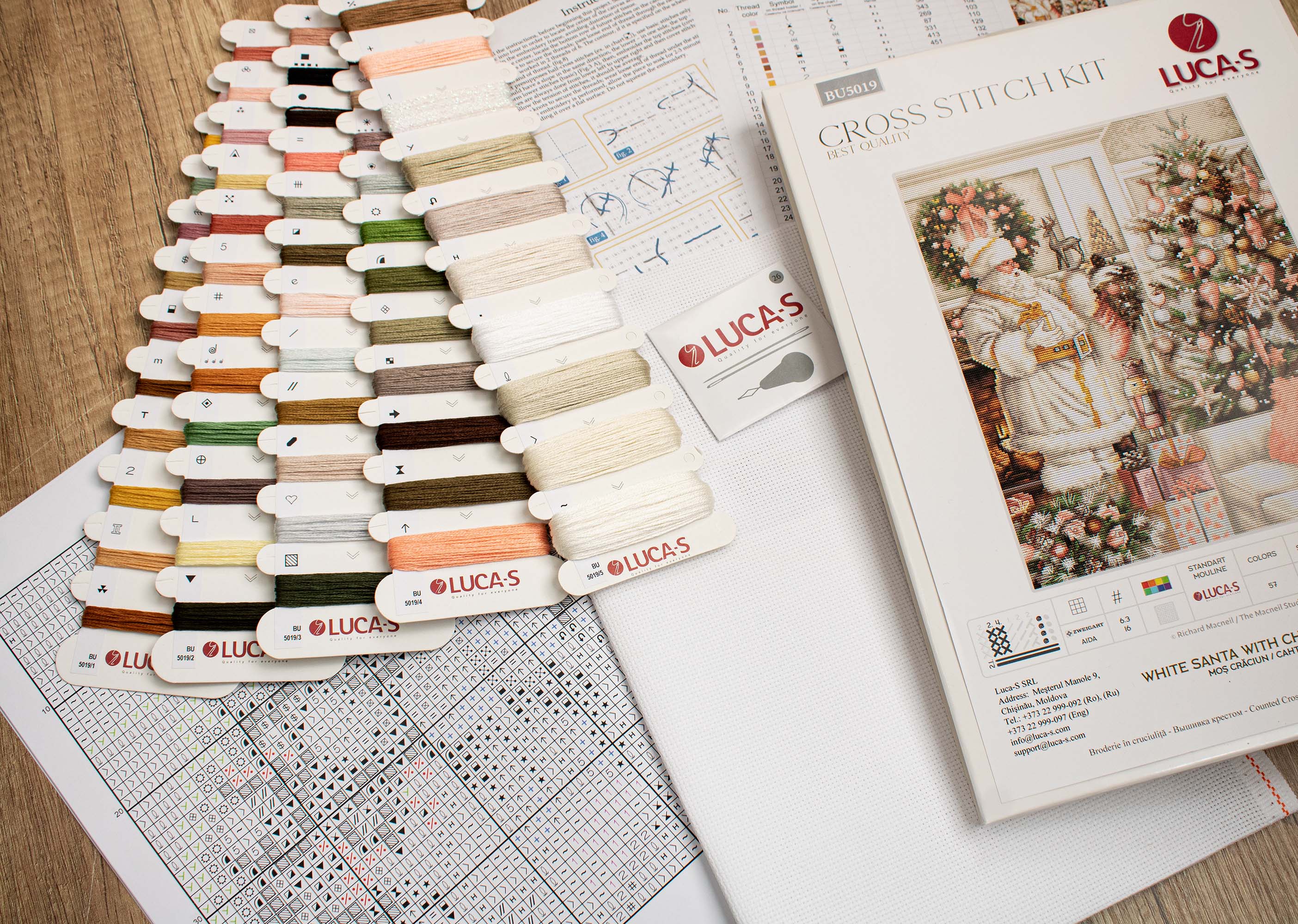 A counted cross-stitch kit featuring a white Santa Claus with a Christmas tree, including Aida canvas, colorful threads, and a needle.