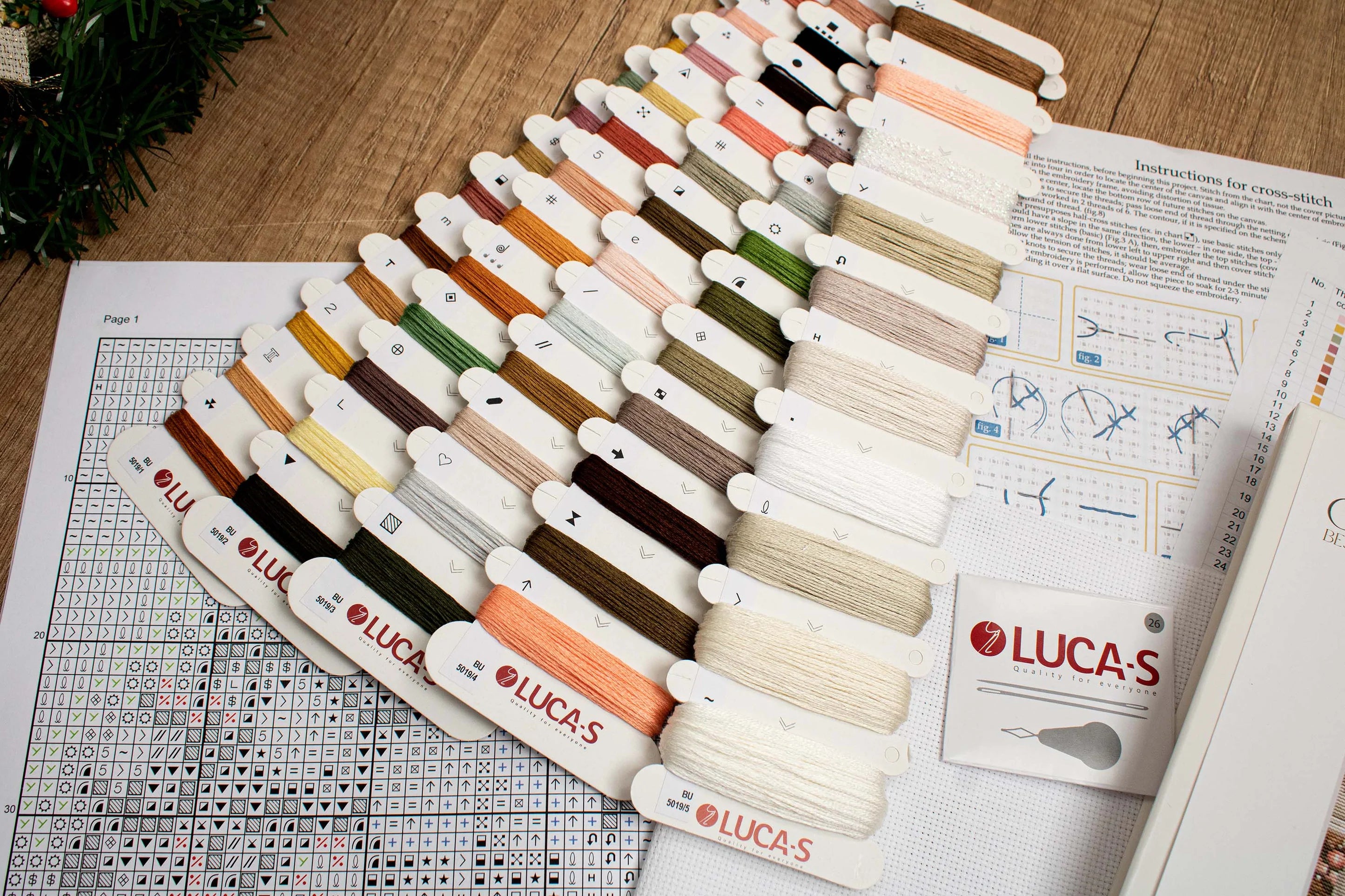 A counted cross-stitch kit featuring a white Santa Claus with a Christmas tree, including Aida canvas, colorful threads, and a needle.