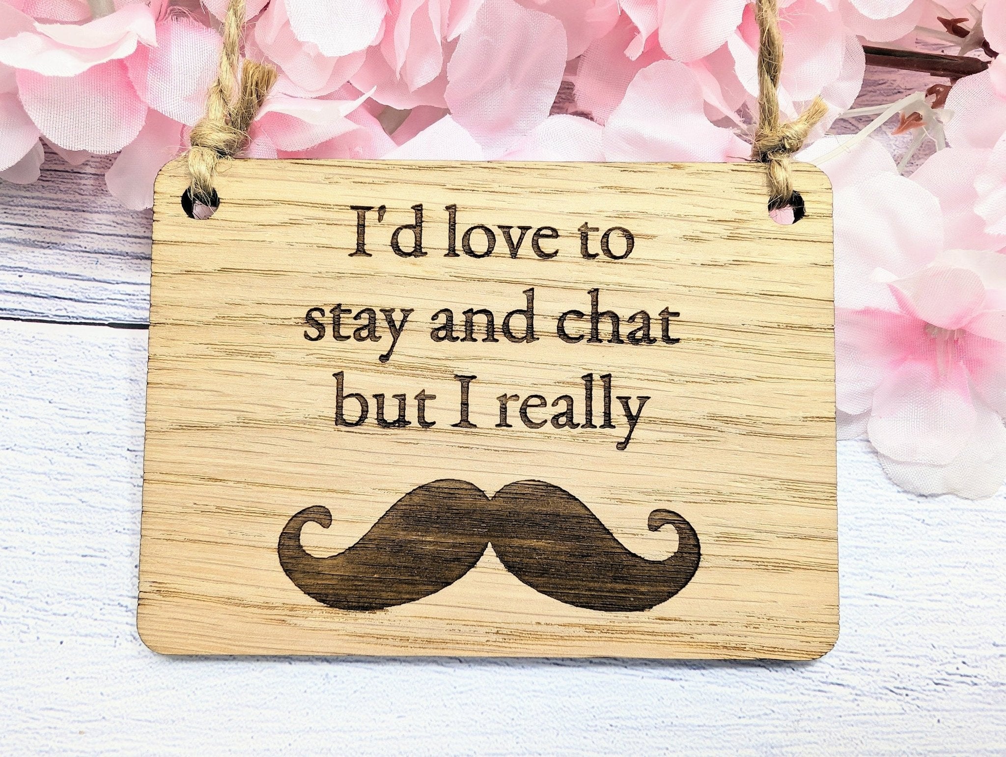 A witty wooden sign featuring the phrase 'I'd Love to Stay and Chat But I Really Moustache' with a quirky moustache illustration, handcrafted from oak veneer.