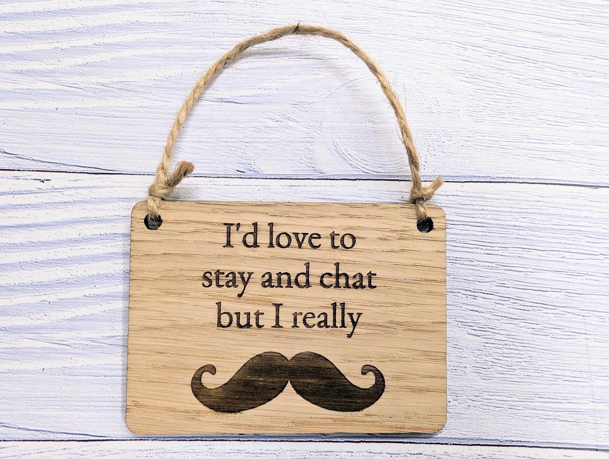 A witty wooden sign featuring the phrase 'I'd Love to Stay and Chat But I Really Moustache' with a quirky moustache illustration, handcrafted from oak veneer.