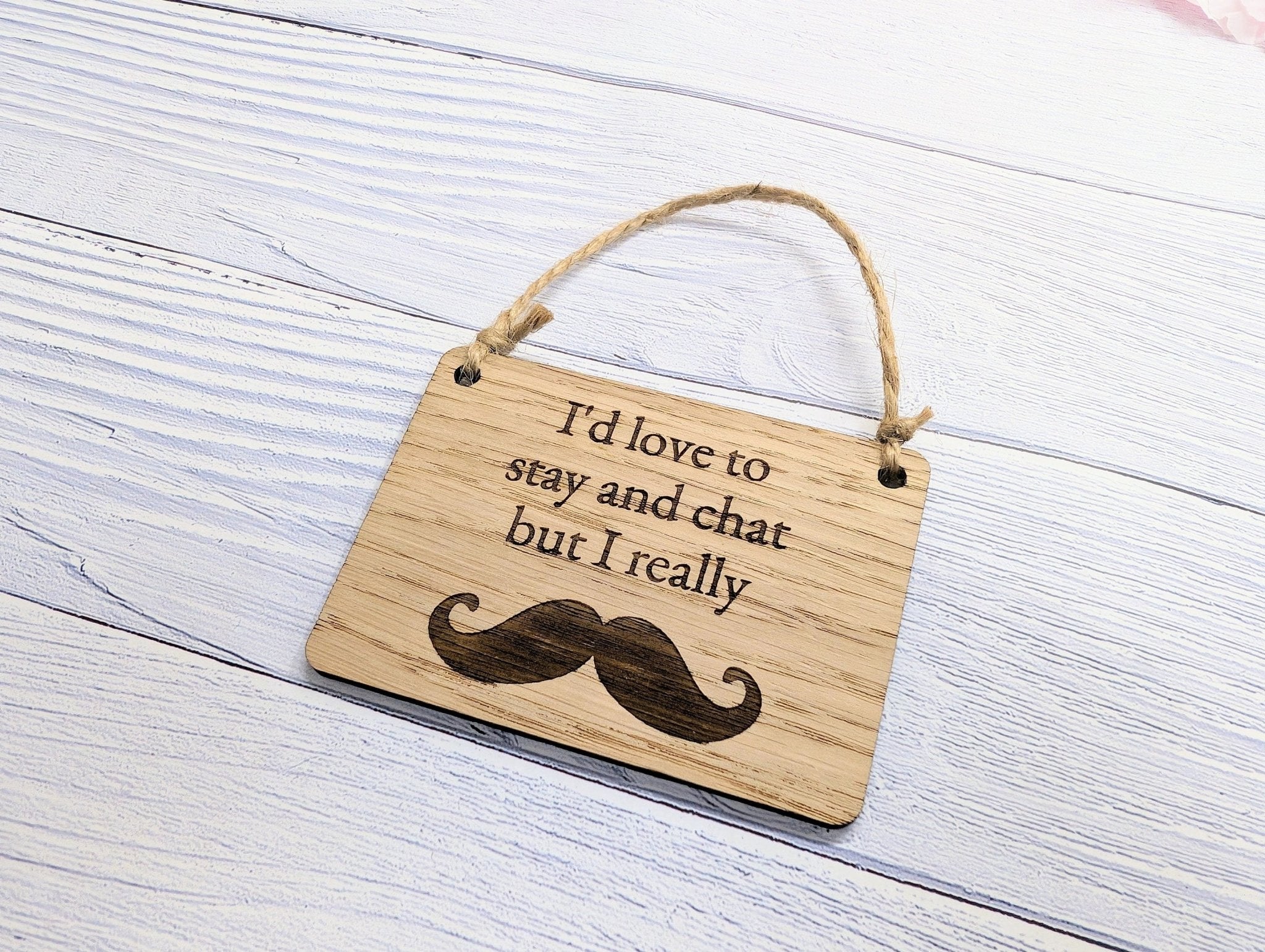 A witty wooden sign featuring the phrase 'I'd Love to Stay and Chat But I Really Moustache' with a quirky moustache illustration, handcrafted from oak veneer.