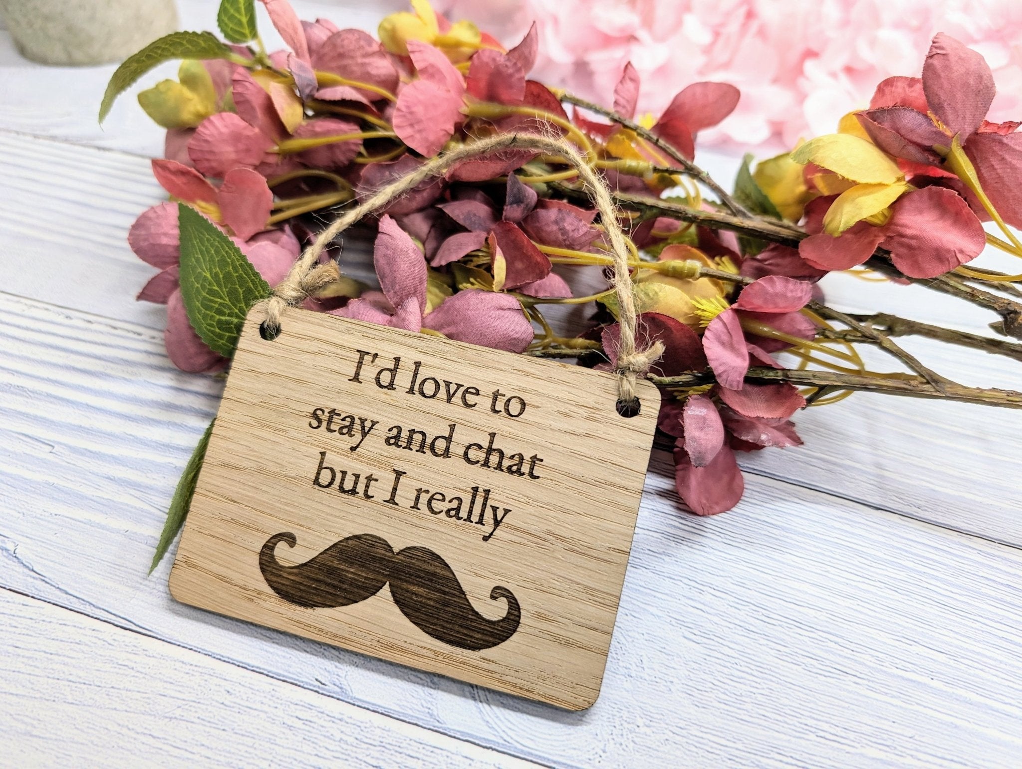 A witty wooden sign featuring the phrase 'I'd Love to Stay and Chat But I Really Moustache' with a quirky moustache illustration, handcrafted from oak veneer.