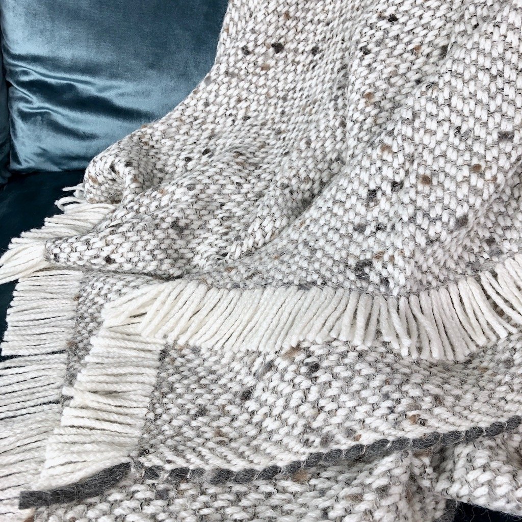 Chunky gray weave alpaca throw blanket draped elegantly on a sofa, showcasing its soft texture and neutral colors.