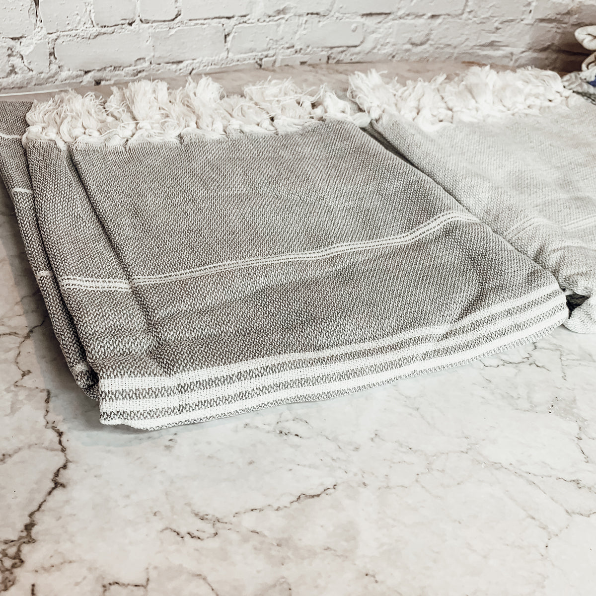 Haley Stripe Towel made from 100% Turkish cotton, featuring decorative tassels and available in light gray and dark gray stripes.