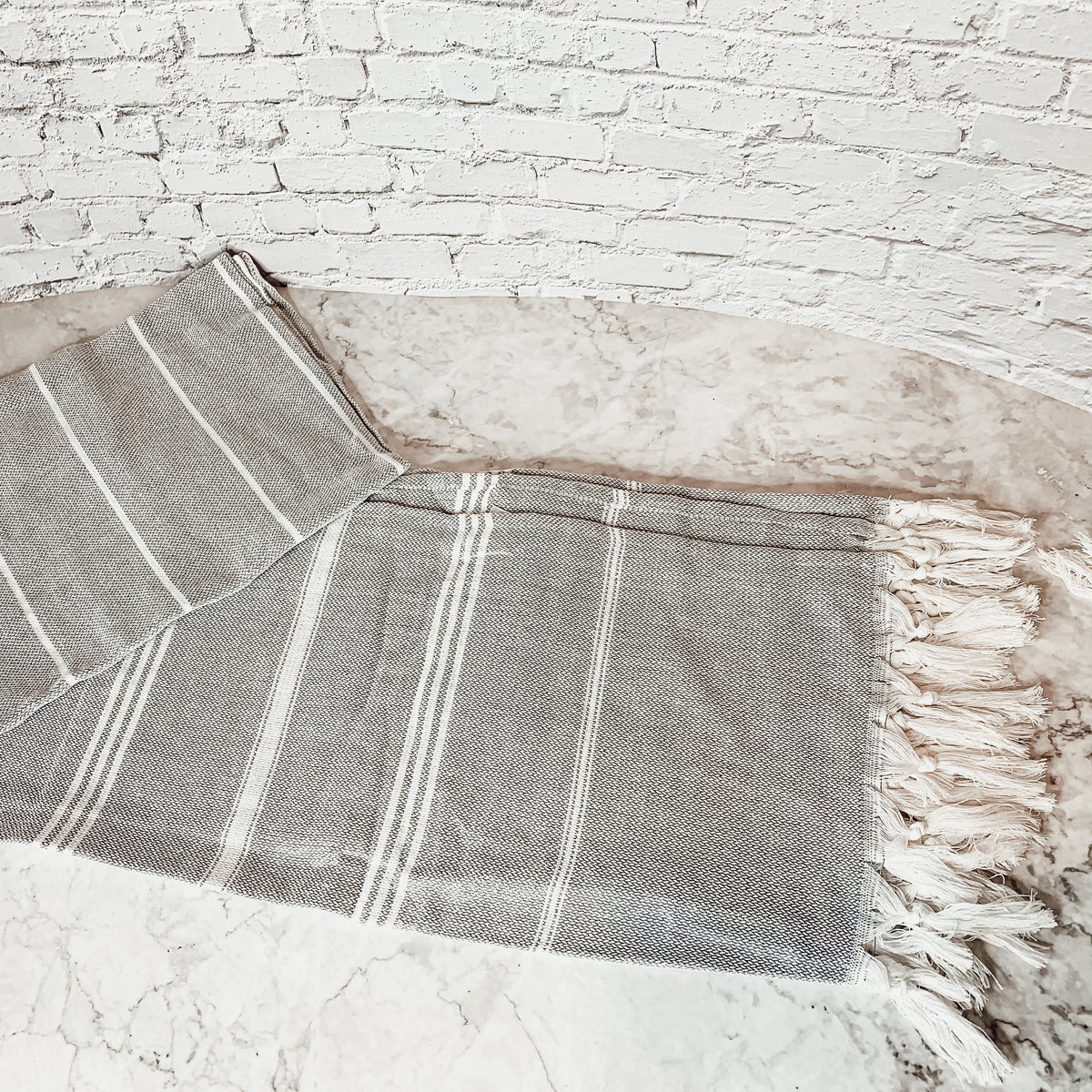 Haley Stripe Towel made from 100% Turkish cotton, featuring decorative tassels and available in light gray and dark gray stripes.