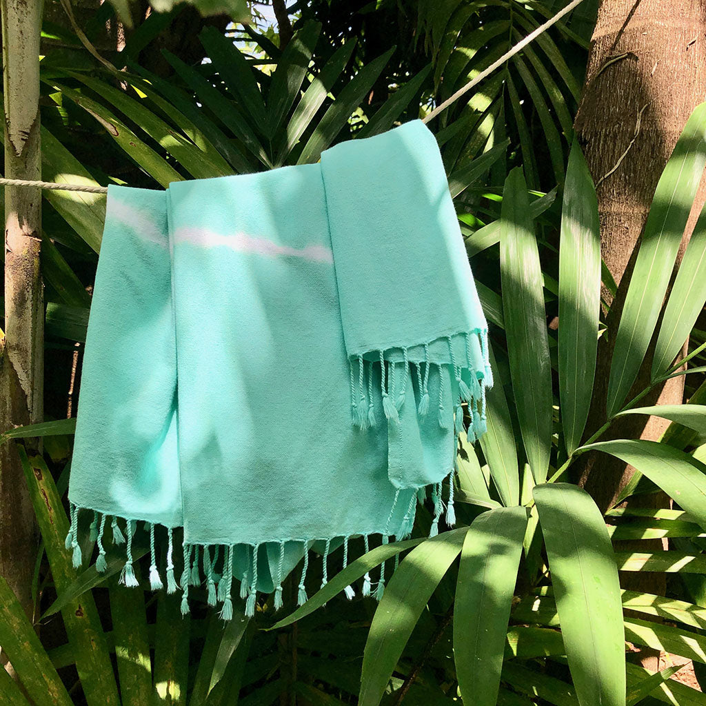 Mint Tie Dye Turkish Beach Towel displayed on a sandy beach, showcasing its vibrant colors and texture.