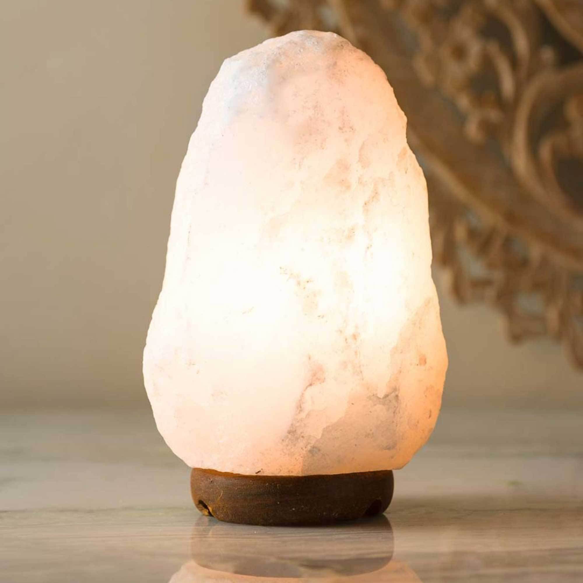 A beautifully shaped Himalayan white salt lamp glowing softly, showcasing its natural rock salt texture and wooden base.