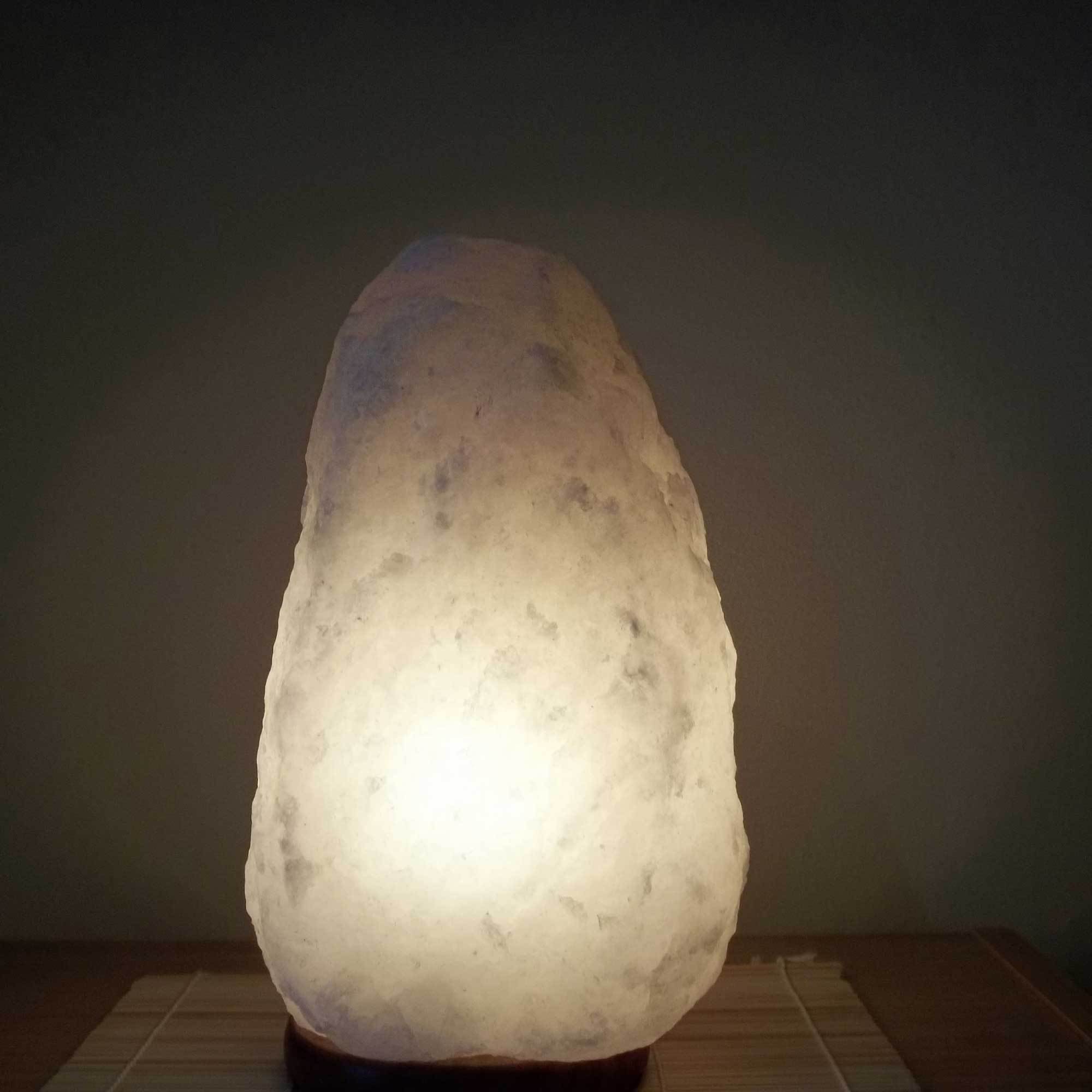 A beautifully shaped Himalayan white salt lamp glowing softly, showcasing its natural rock salt texture and wooden base.