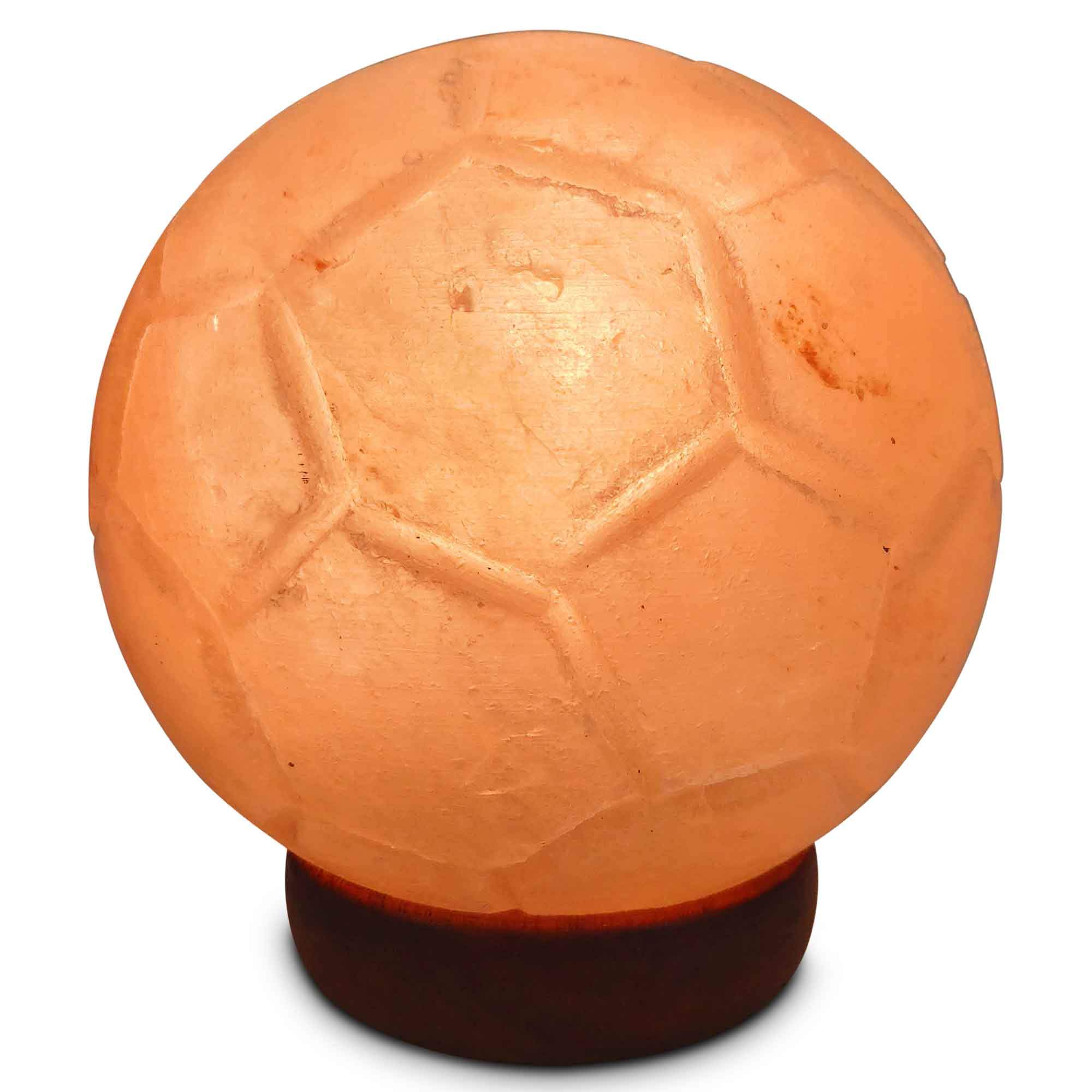 A beautifully carved Himalayan pink salt lamp in the shape of a soccer ball, glowing softly on a wooden base.