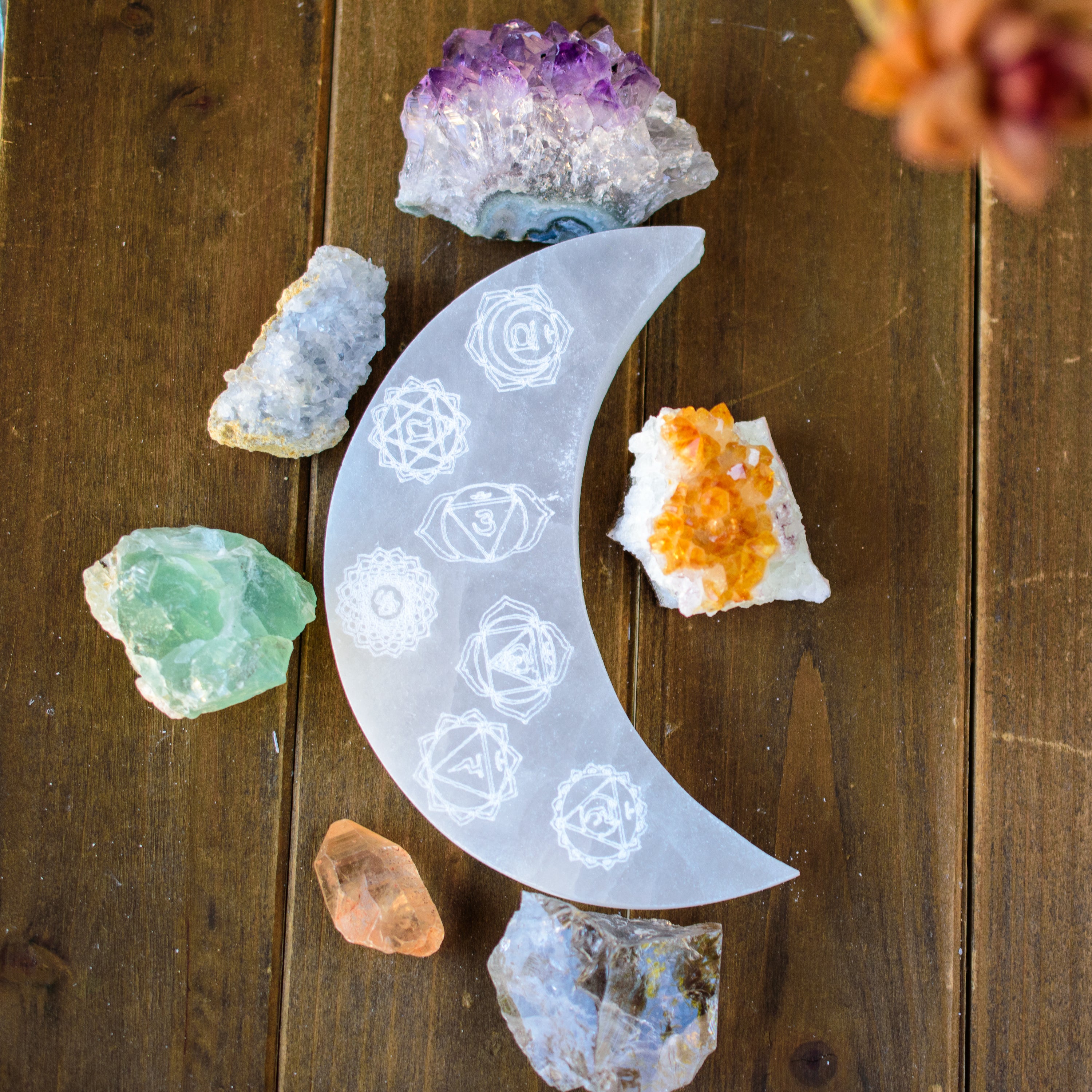 A beautifully hand-carved crescent moon selenite plate engraved with the 7 chakra symbols, showcasing its polished surface and unique design.