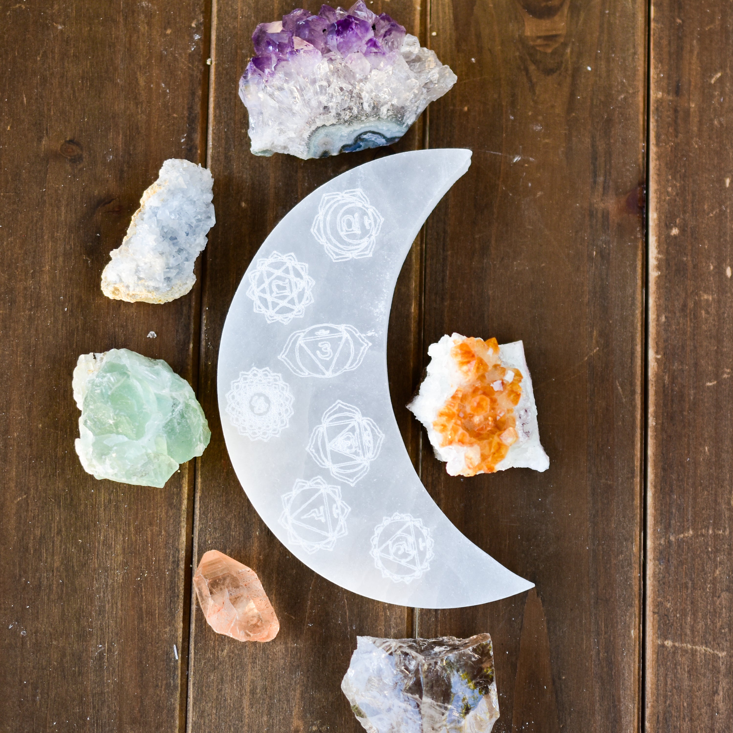 A beautifully hand-carved crescent moon selenite plate engraved with the 7 chakra symbols, showcasing its polished surface and unique design.