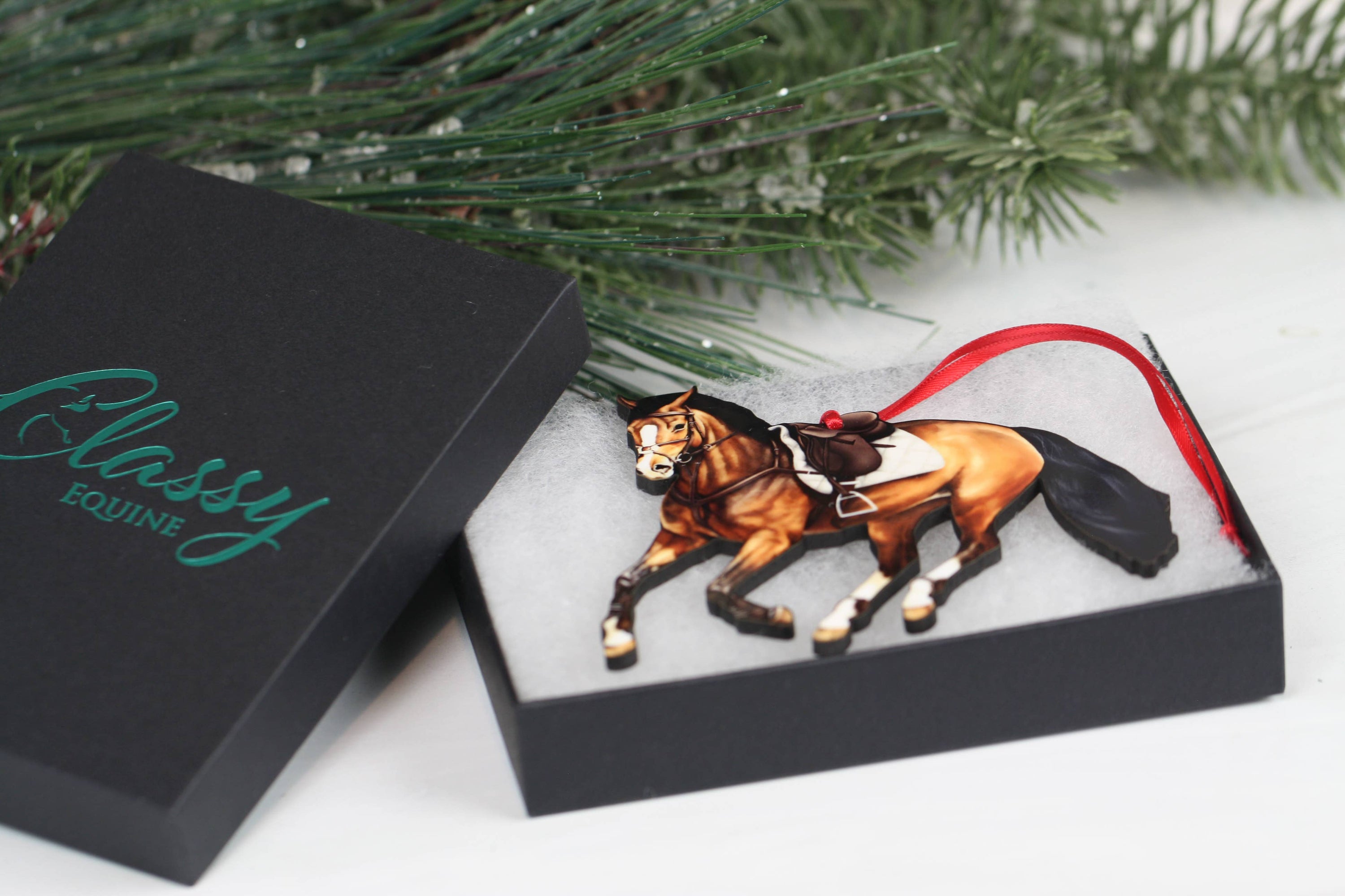 A beautifully crafted bay galloping jumper horse ornament made of composite wood, featuring red and black ribbons, perfect for Christmas and year-round display.