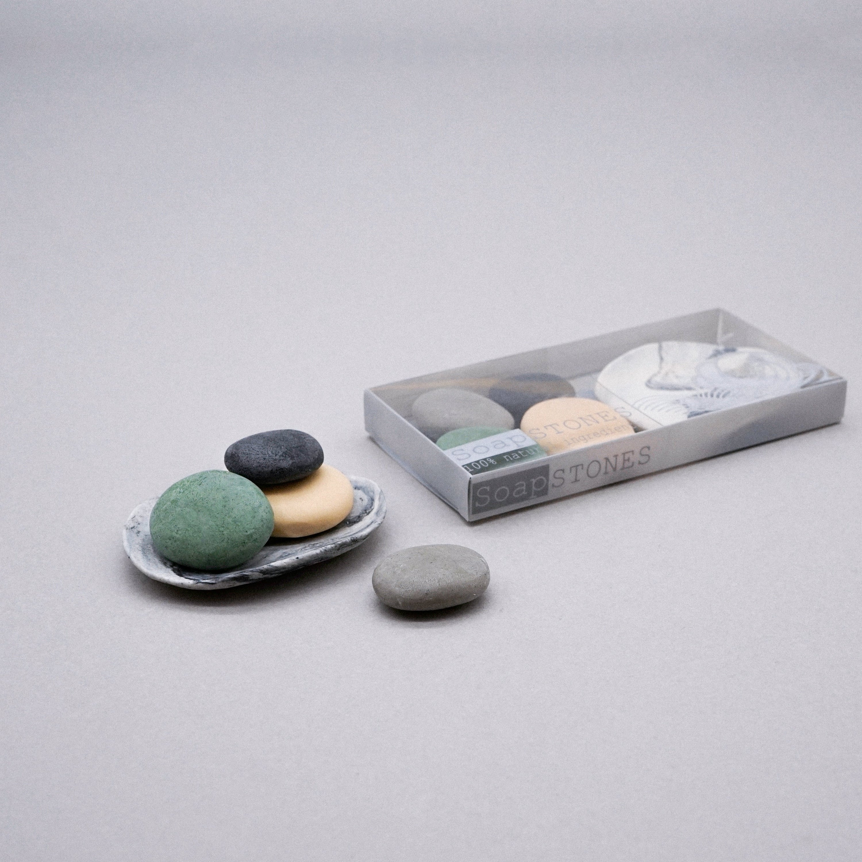 A set of assorted handmade big pebble soaps in a white porcelain dish with a marble effect design, showcasing their natural beauty.