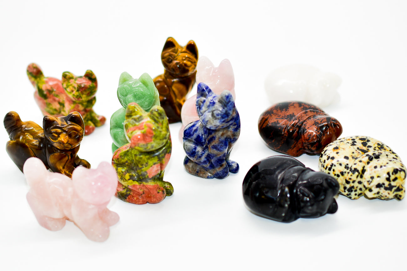A collection of beautifully crafted cat crystal carvings in various poses, made from natural stones like Rose Quartz and Tiger's Eye.