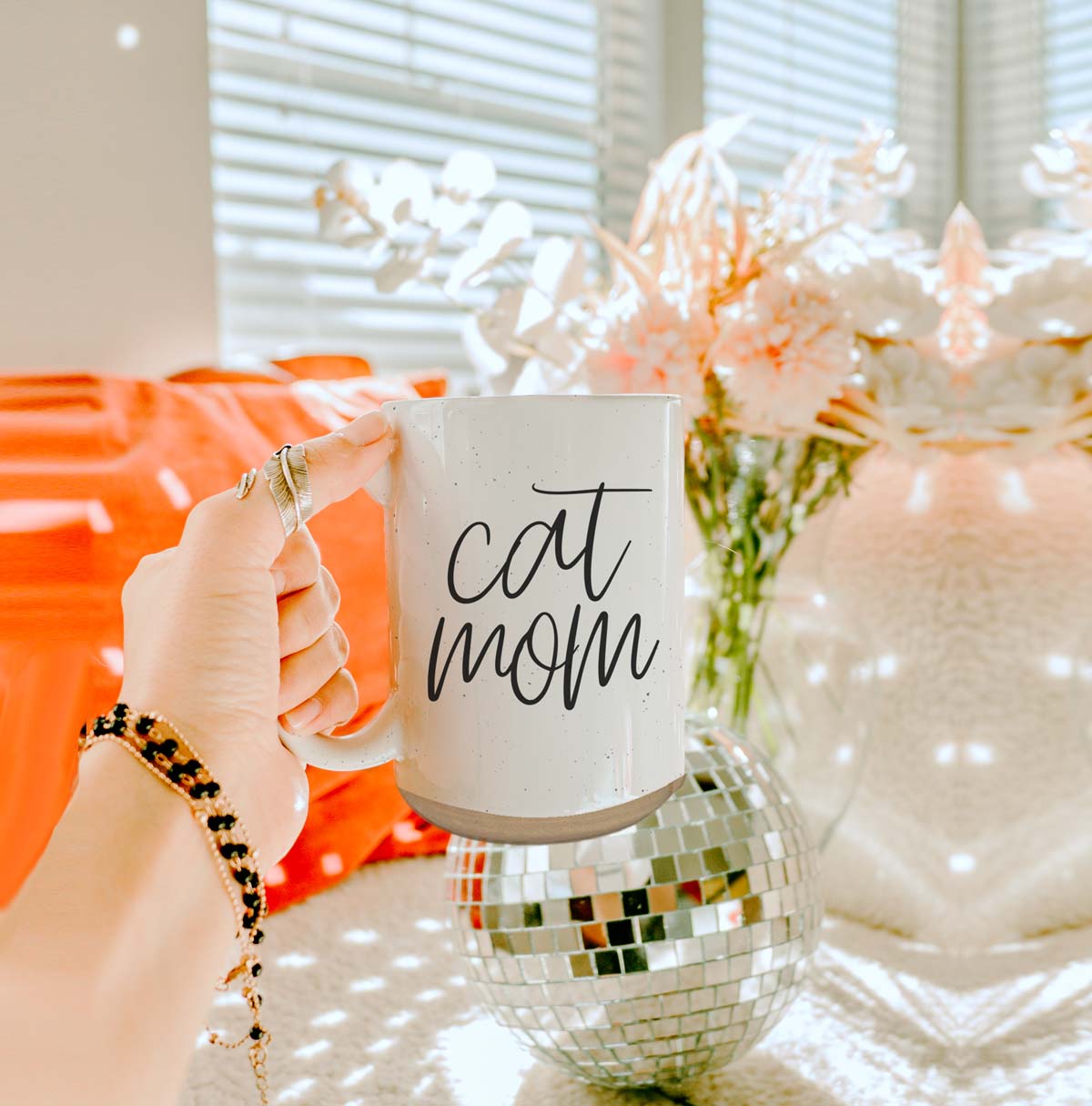 A stylish off-white ceramic mug with dark speckles, featuring a black graphic that reads 'Cat Mom' on both sides, perfect for cat lovers.