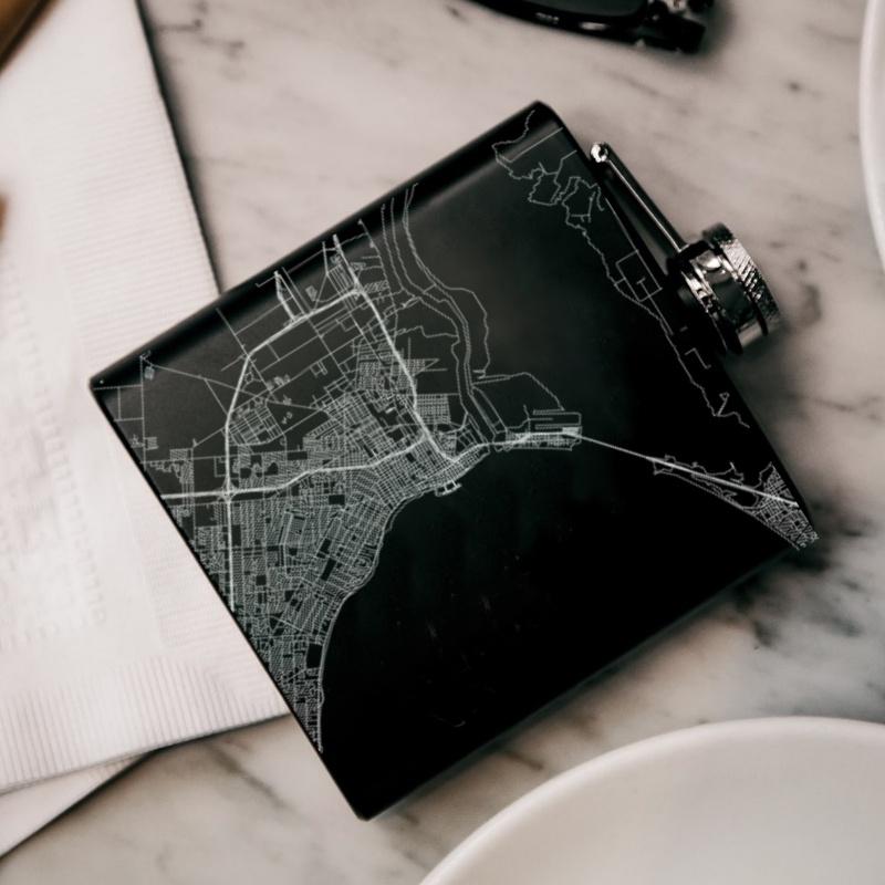 Custom engraved matte black hip flask featuring a map of Corpus Christi, Texas with coordinates, accompanied by a canvas bag and funnel.