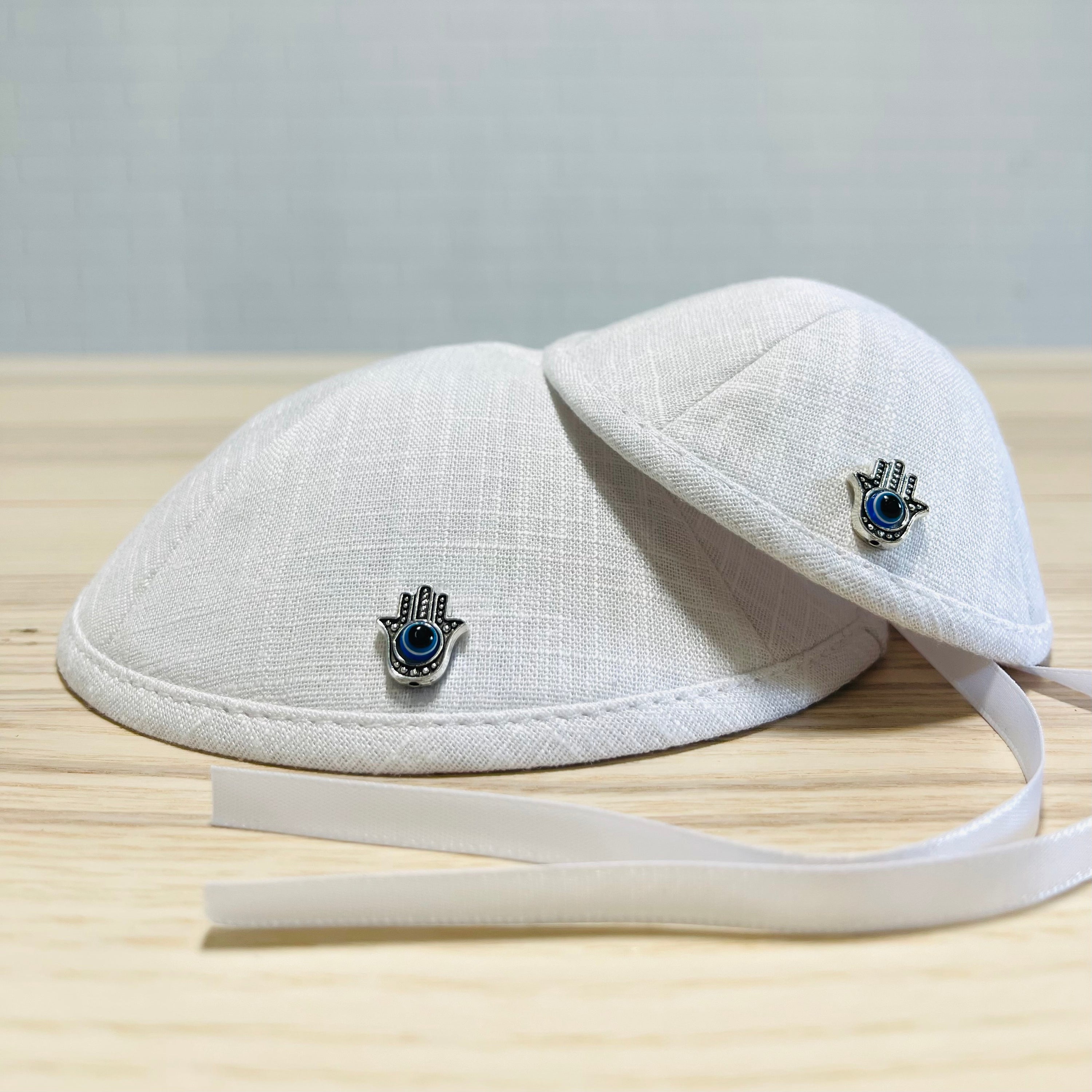 Father and baby boy wearing matching Hamsa linen kippahs for Brit Milah, showcasing elegant design and teddy bear embroidery.