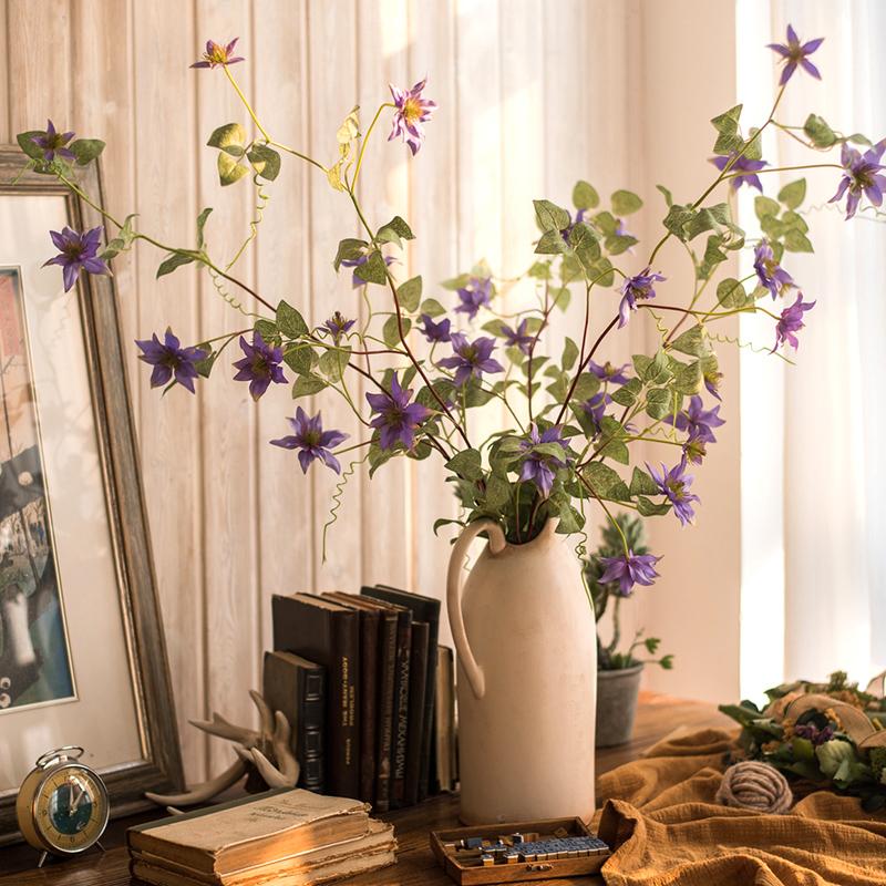 A 40-inch tall faux silk clematis flower stem in purple, featuring seven realistic blooms and lush green foliage, perfect for home decor.