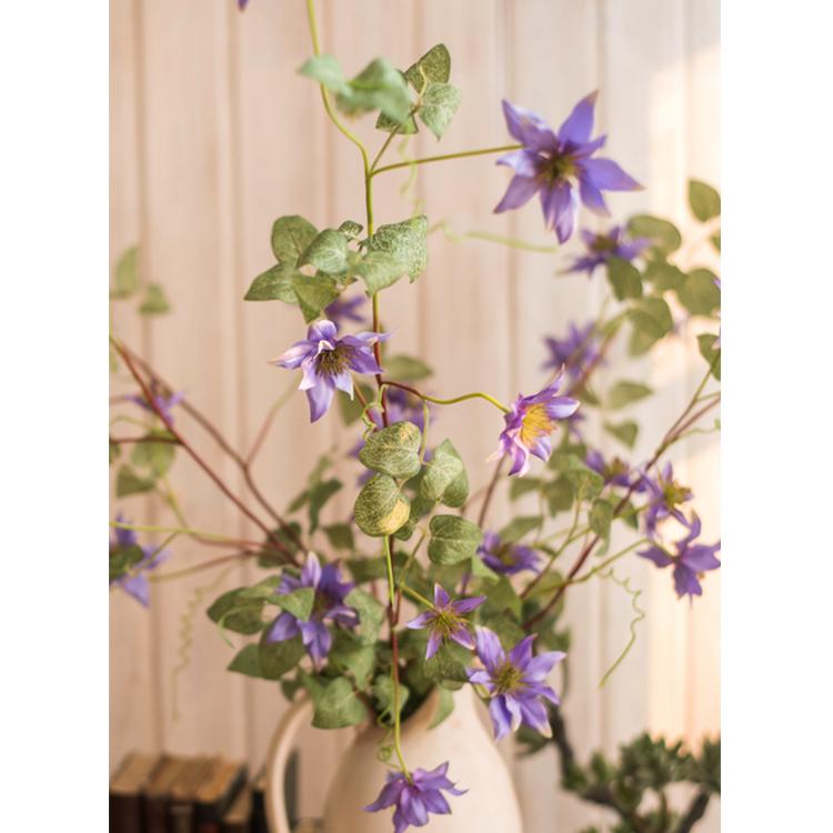 A 40-inch tall faux silk clematis flower stem in purple, featuring seven realistic blooms and lush green foliage, perfect for home decor.