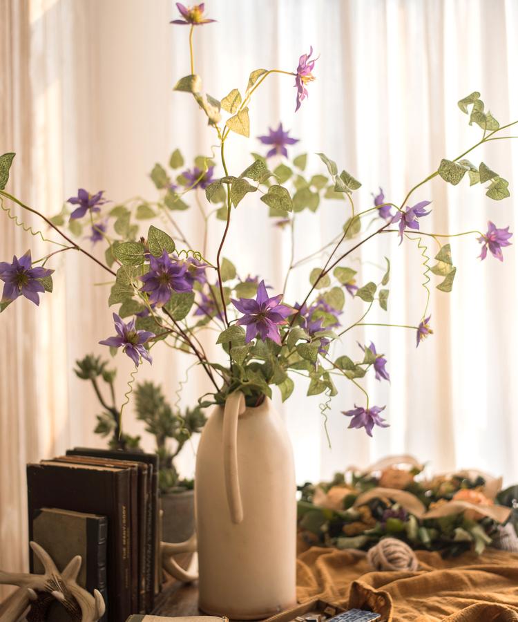 A 40-inch tall faux silk clematis flower stem in purple, featuring seven realistic blooms and lush green foliage, perfect for home decor.