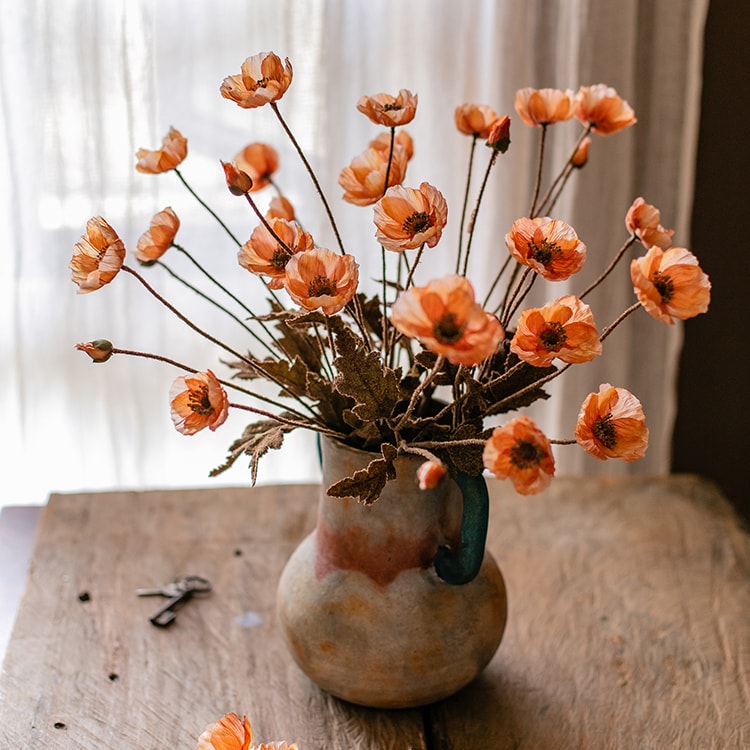 A vibrant orange faux silk poppy flower stem, 23 inches tall, featuring three blooms and one bud, with green leaves.