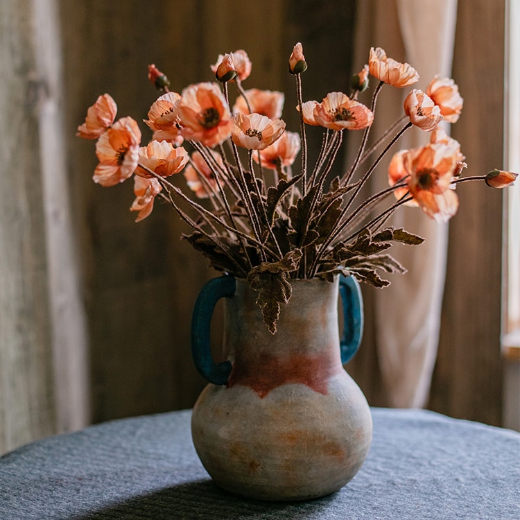A vibrant orange faux silk poppy flower stem, 23 inches tall, featuring three blooms and one bud, with green leaves.