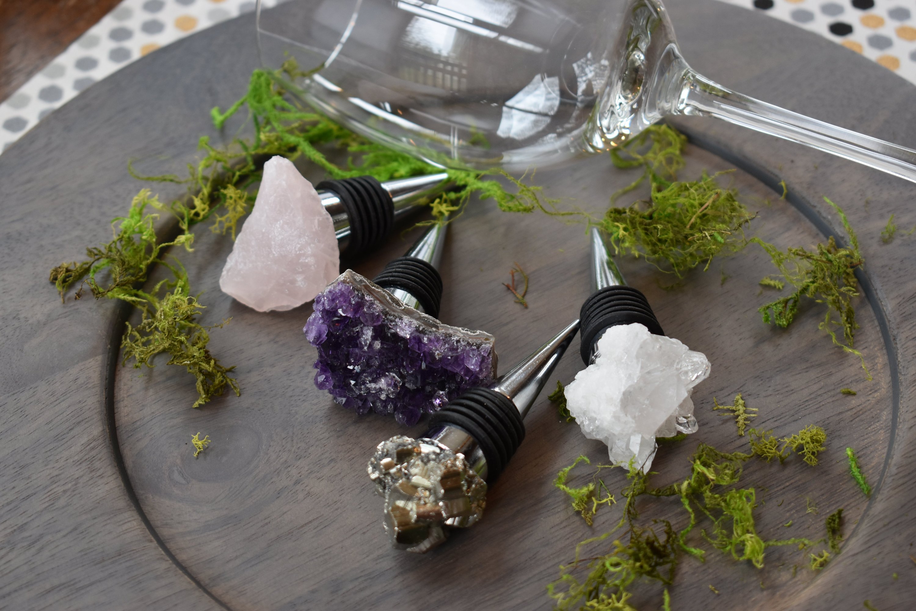 Elegant gemstone wine stoppers with stainless steel base and silicone seal, featuring rose quartz, white quartz, amethyst, and pyrite options.