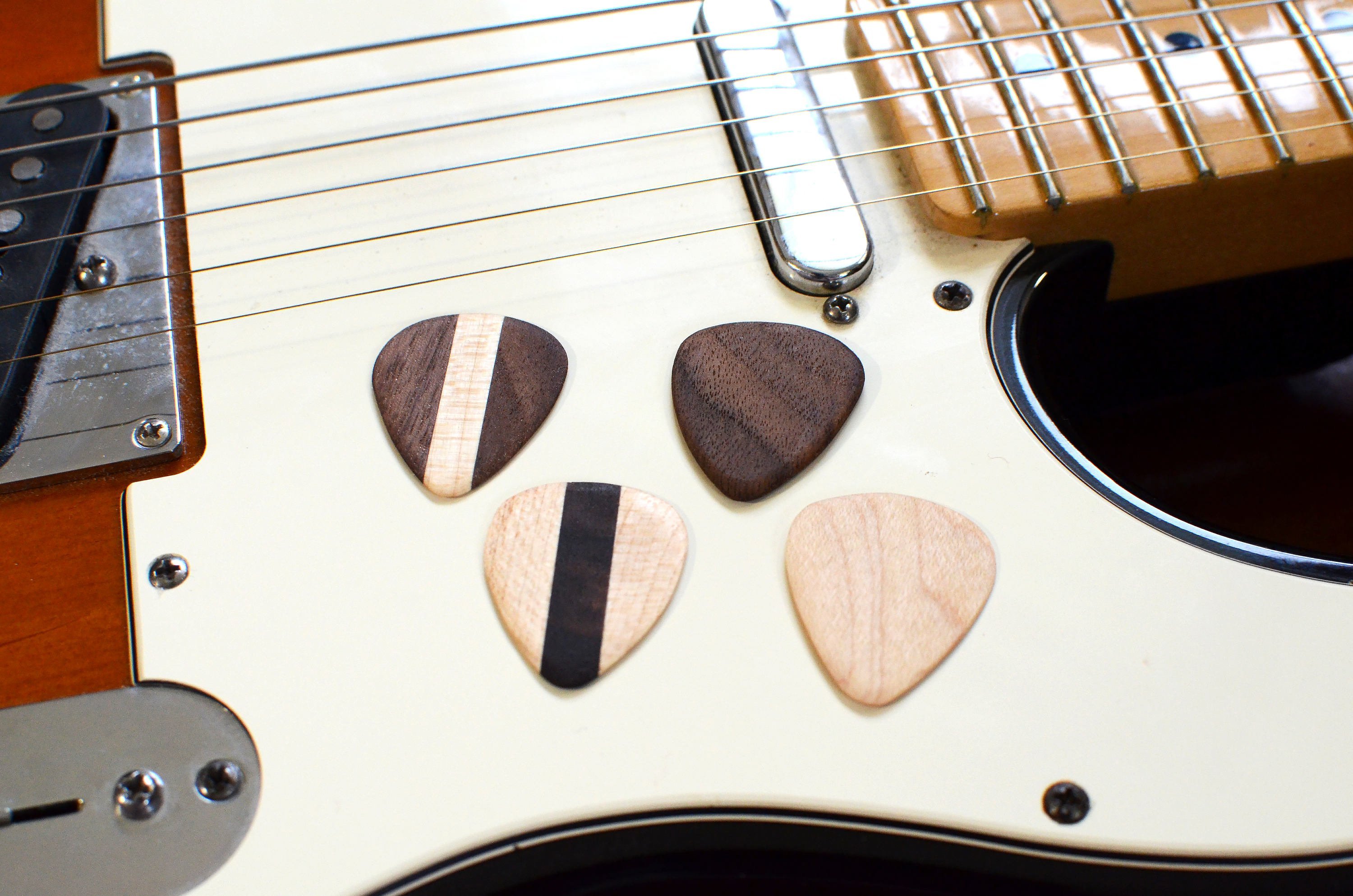 Set of 4 handcrafted hardwood guitar picks made from Black Walnut and Maple, showcasing their natural finish and unique grain patterns.