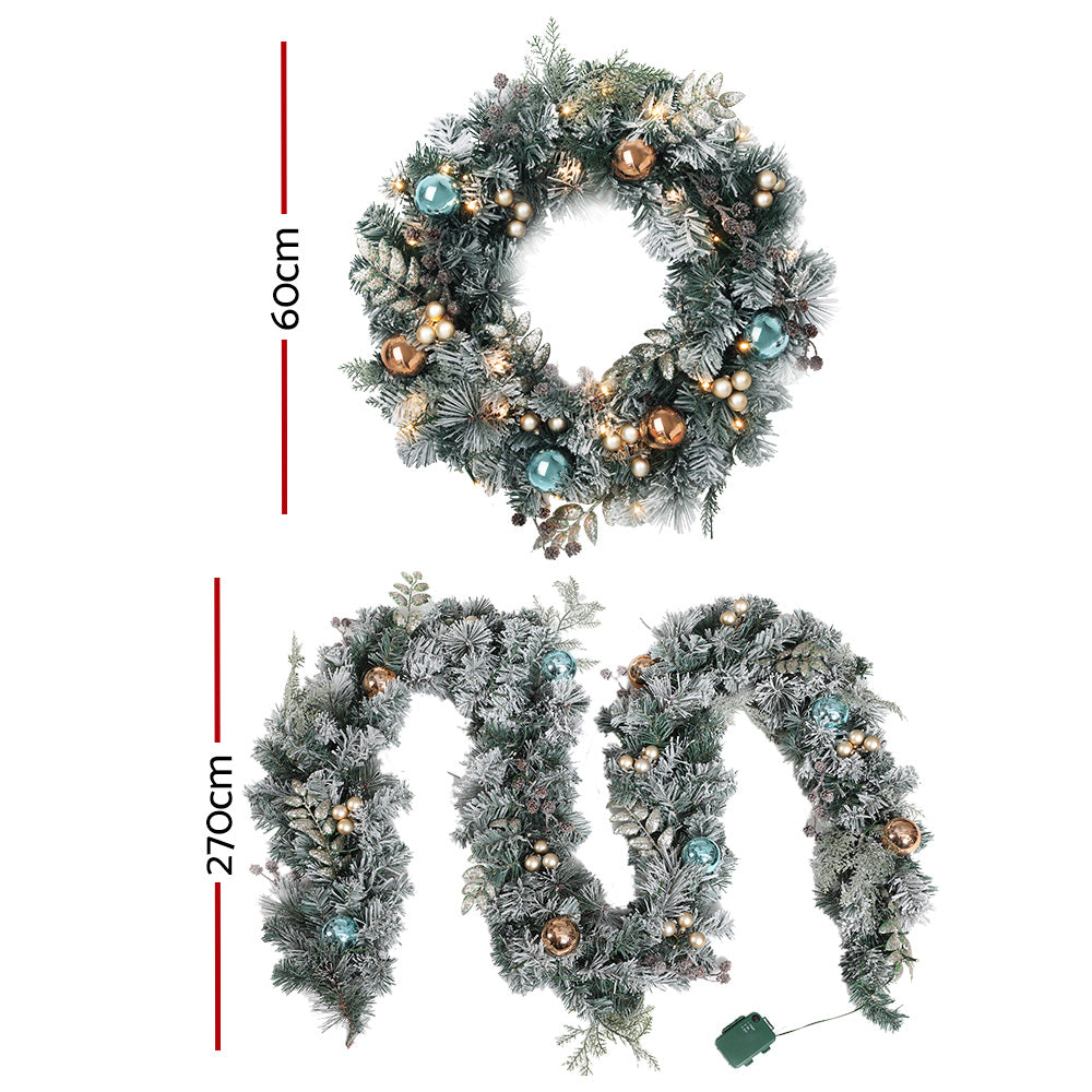Jingle Jollys Christmas Garland and Wreath set featuring snow-frosted foliage, warm LED lights, and decorative pine cones.