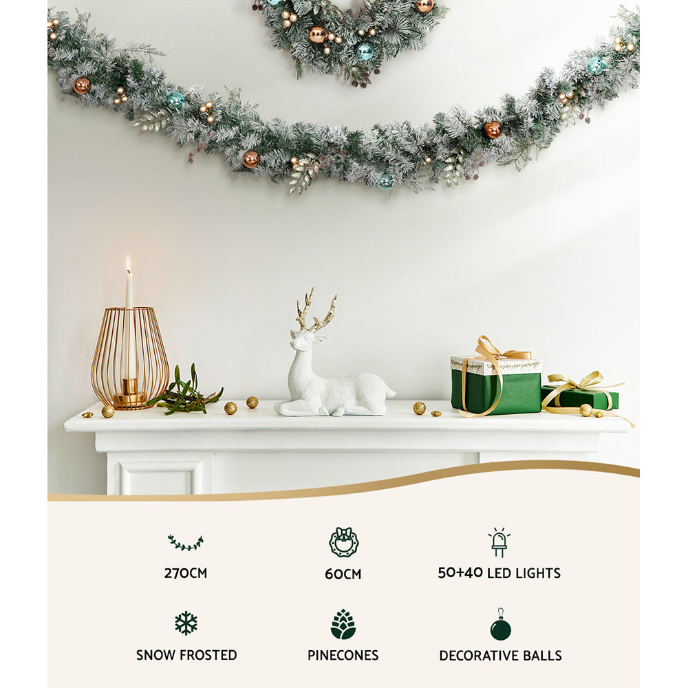 Jingle Jollys Christmas Garland and Wreath set featuring snow-frosted foliage, warm LED lights, and decorative pine cones.