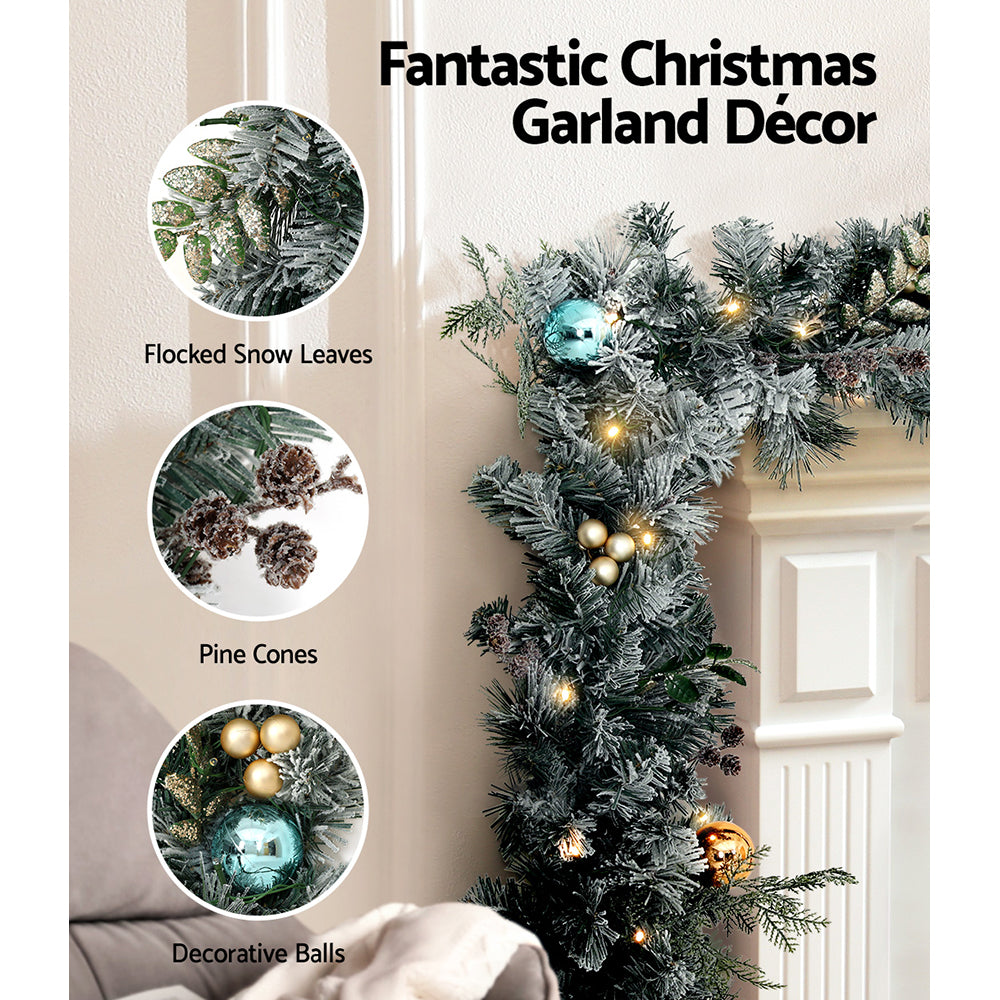 Jingle Jollys Christmas Garland and Wreath set featuring snow-frosted foliage, warm LED lights, and decorative pine cones.