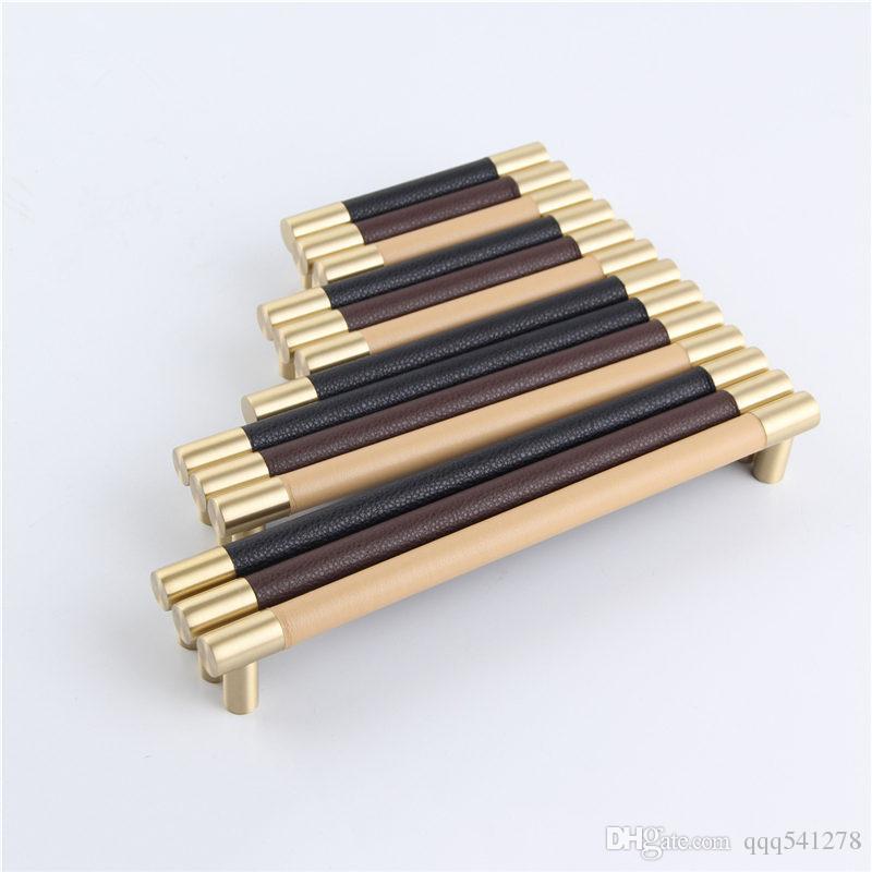 Stylish leather and brass furniture handles for cabinets and drawers, showcasing a brushed gold finish.