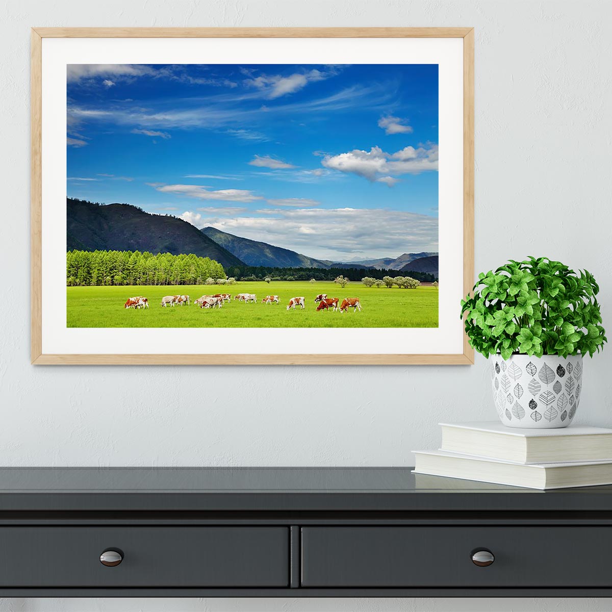 A framed print of a mountain landscape featuring grazing cows under a clear blue sky, showcasing vibrant colors and exquisite craftsmanship.