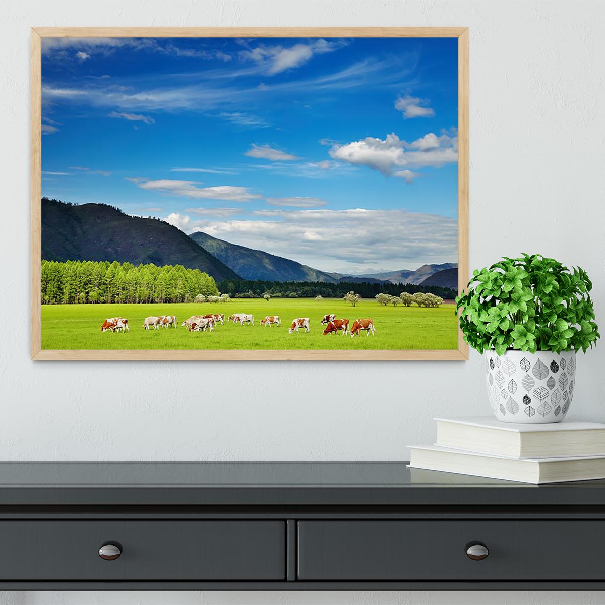 A framed print of a mountain landscape featuring grazing cows under a clear blue sky, showcasing vibrant colors and exquisite craftsmanship.