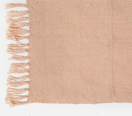 A pastel pink acrylic throw with detailed tassels, handwoven by artisans, showcasing a unique design.