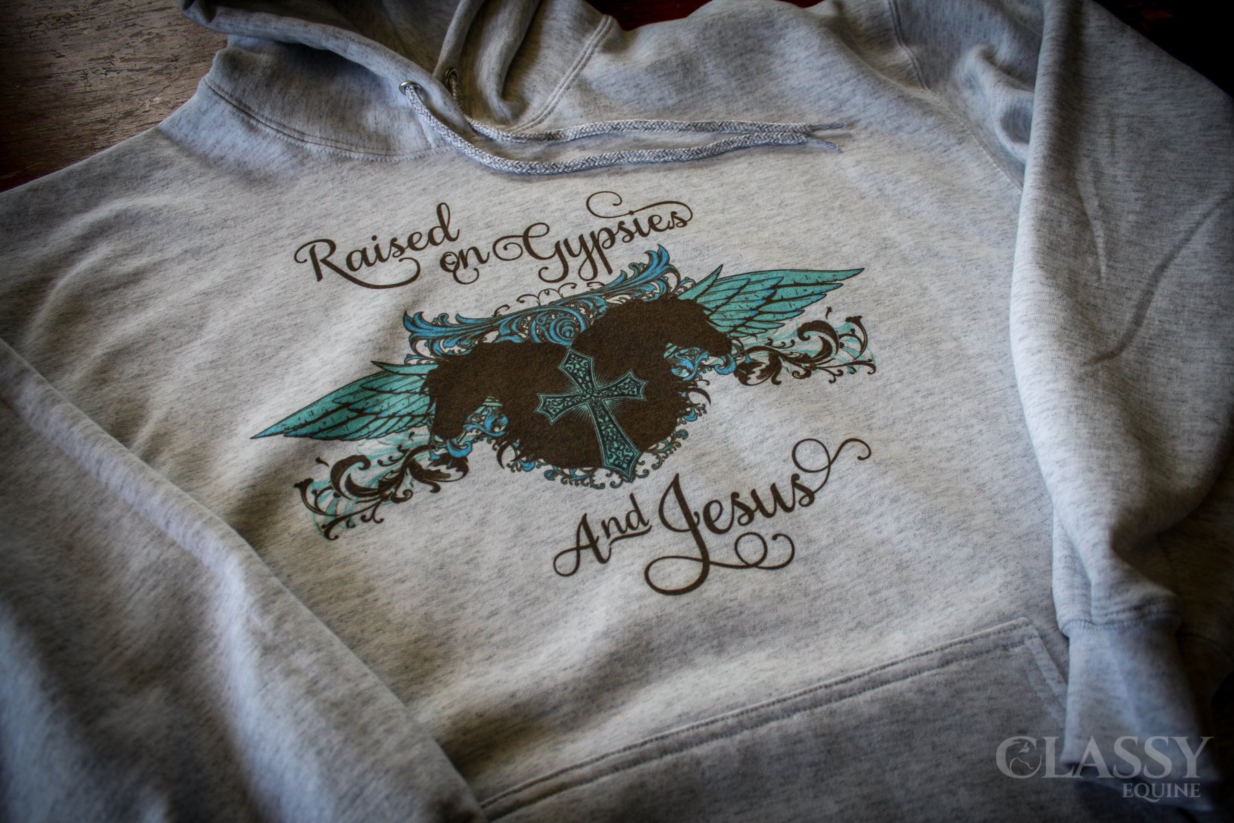 A cozy ash gray hooded sweatshirt featuring the phrase 'Raised on Gypsies and Jesus', perfect for casual wear.