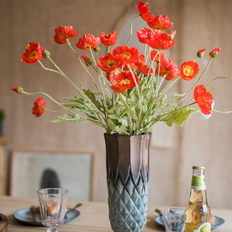 A 22-inch tall Silk Common Poppy Flower Stem featuring vibrant orange, red, and yellow blooms with green leaves, perfect for home decor.