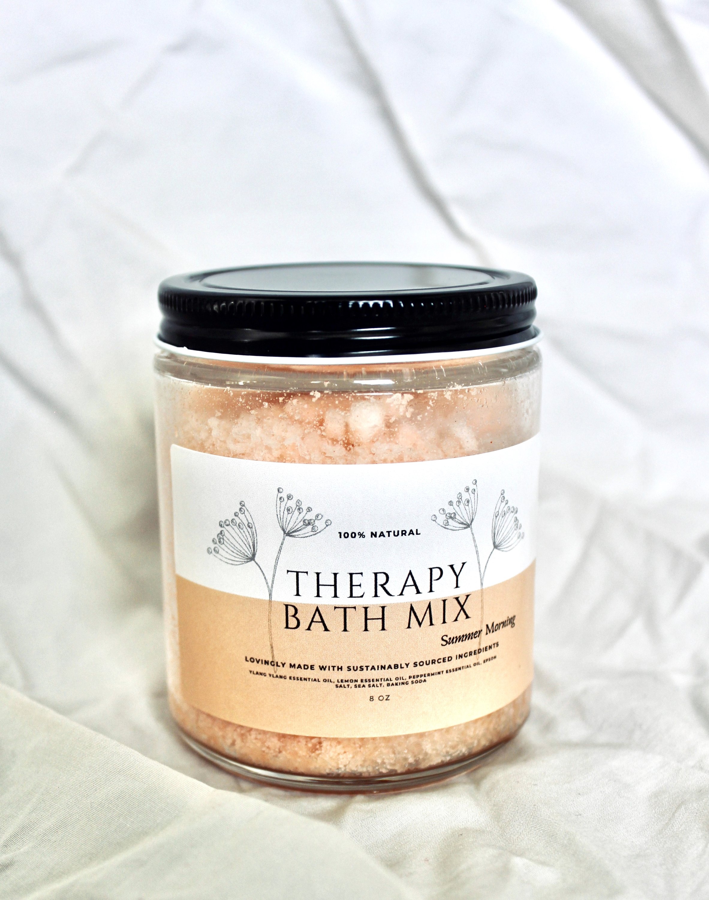 A jar of Summer Morning Therapy Bath Mix with ylang ylang, lemon, and peppermint, surrounded by fresh summer flowers.