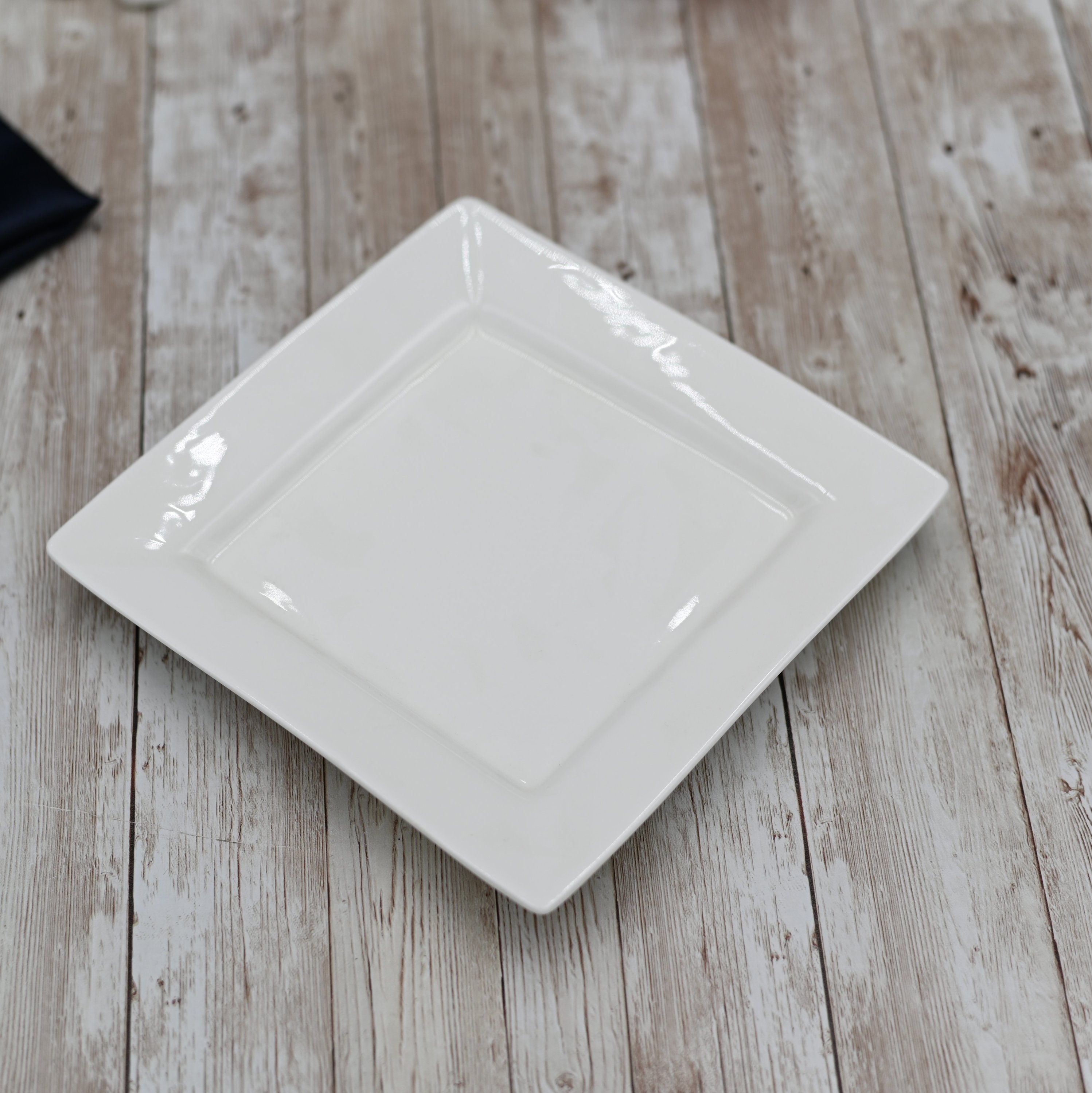 A square white dinner plate made of fine porcelain, showcasing its elegant design and smooth surface, perfect for any dining occasion.