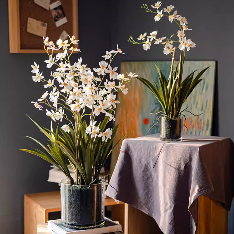 A beautiful White Hui Lan Orchid in a stylish glass pot, showcasing realistic silk petals and lush green leaves.