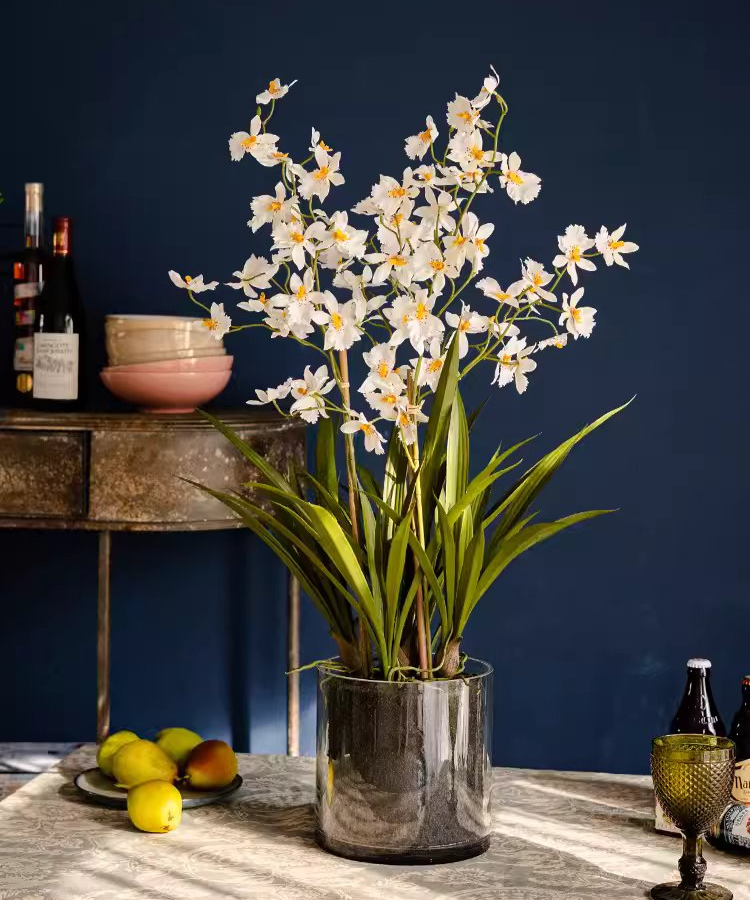 A beautiful White Hui Lan Orchid in a stylish glass pot, showcasing realistic silk petals and lush green leaves.