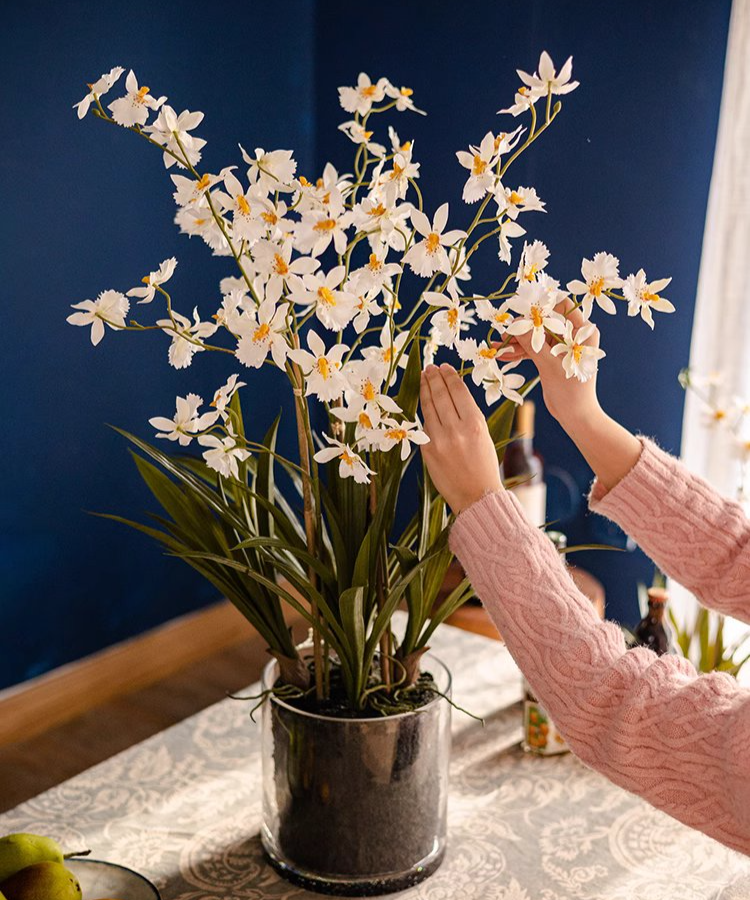 A beautiful White Hui Lan Orchid in a stylish glass pot, showcasing realistic silk petals and lush green leaves.
