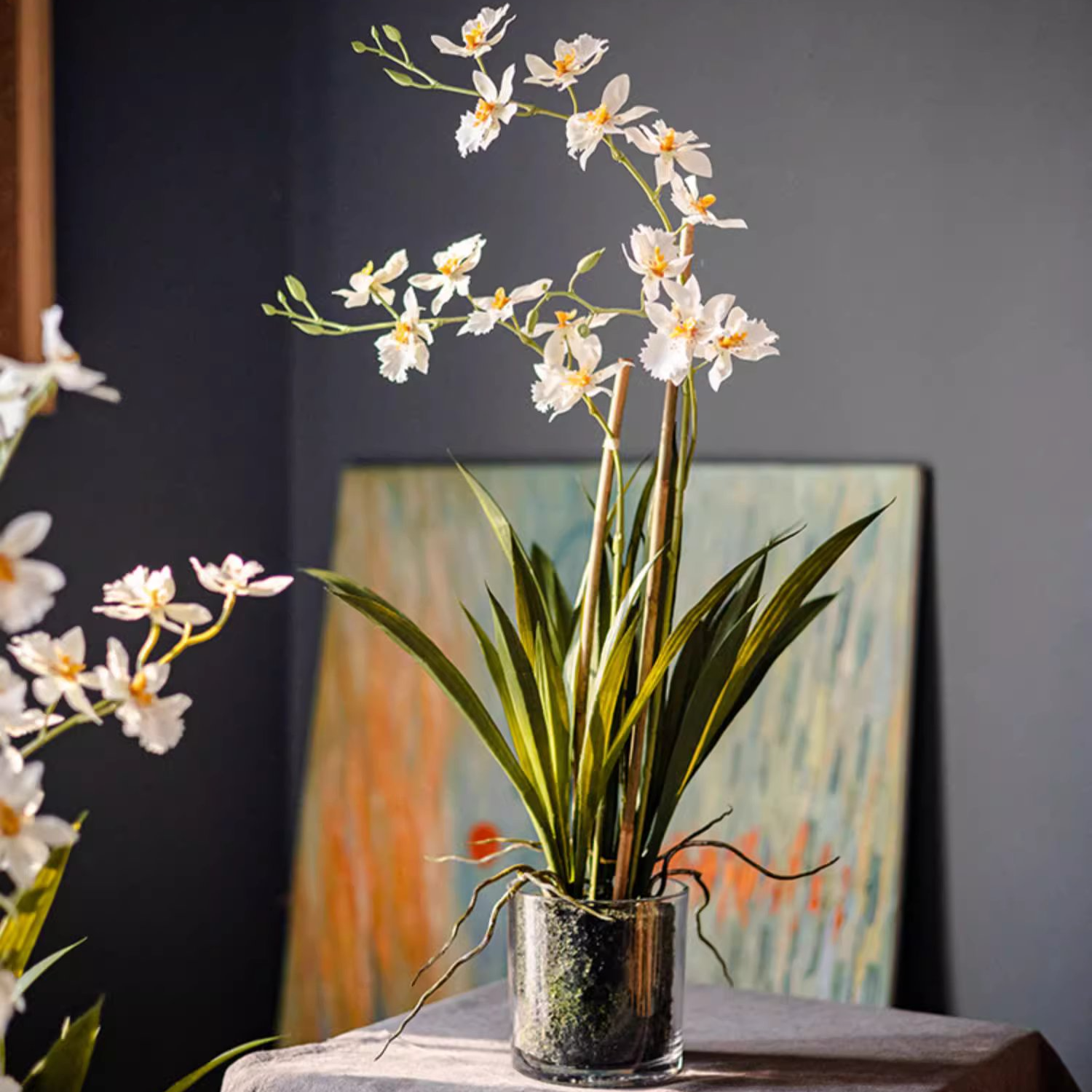 A beautiful White Hui Lan Orchid in a stylish glass pot, showcasing realistic silk petals and lush green leaves.