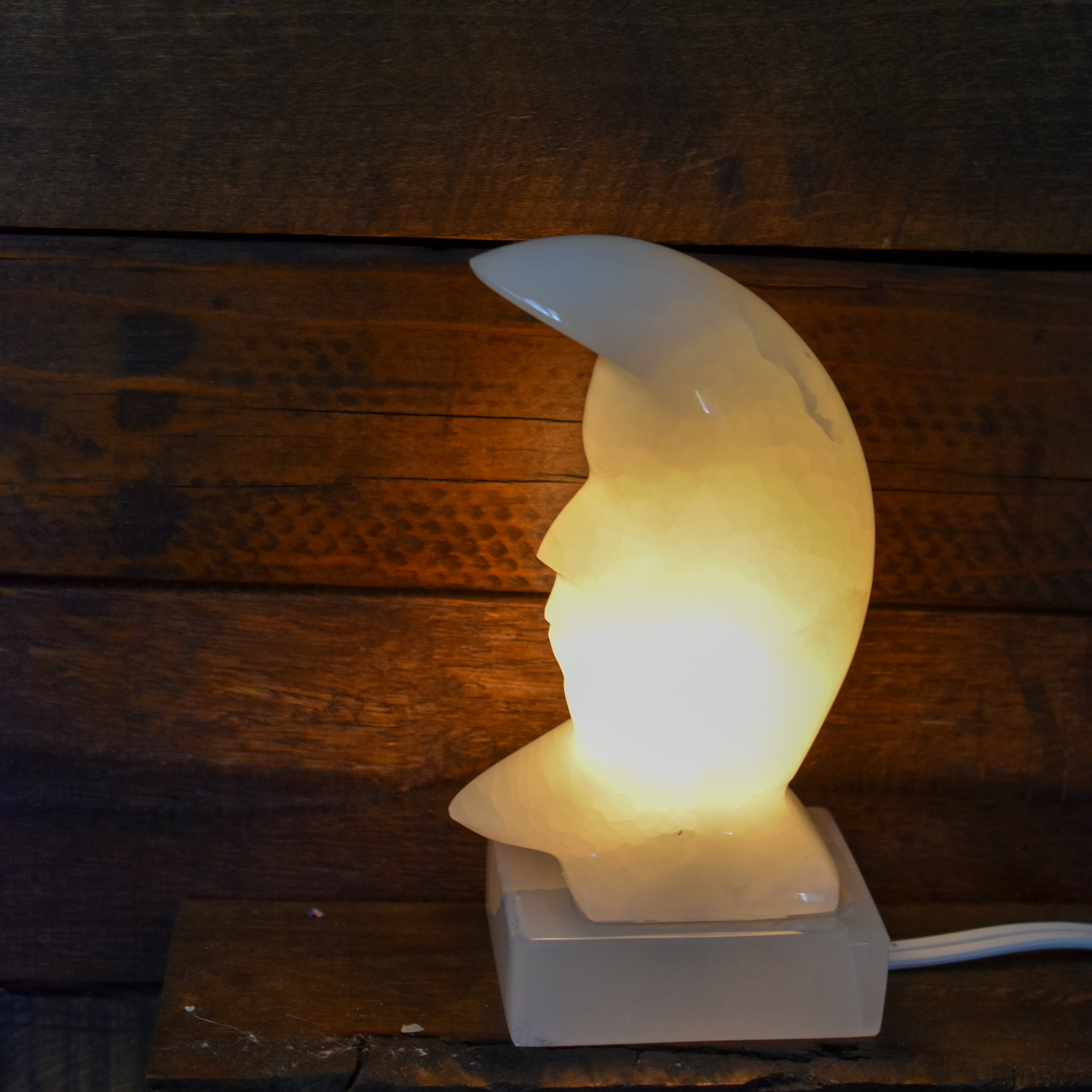A beautifully crafted white onyx crescent moon lamp, hand carved and polished, showcasing intricate details and a warm glow.