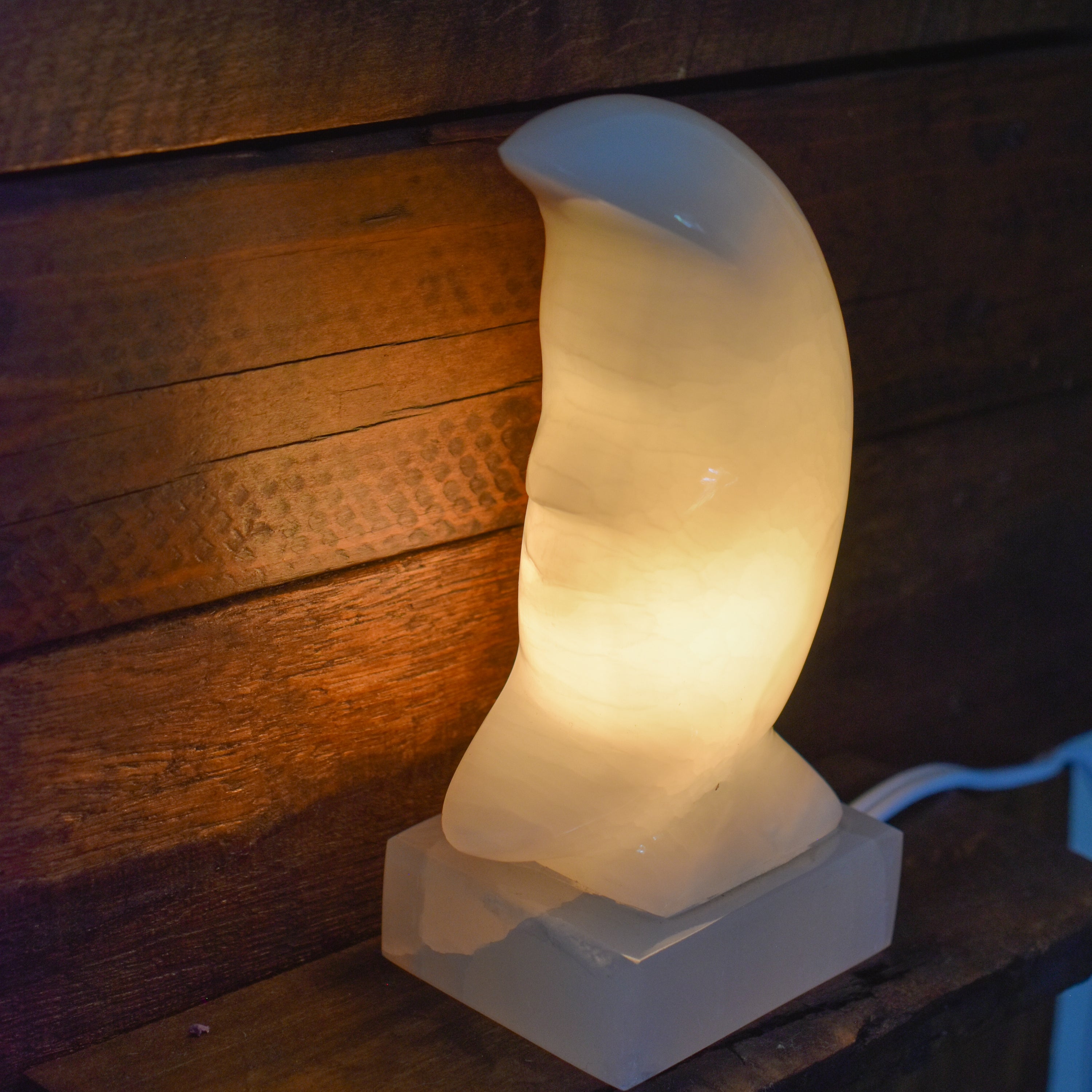 A beautifully crafted white onyx crescent moon lamp, hand carved and polished, showcasing intricate details and a warm glow.