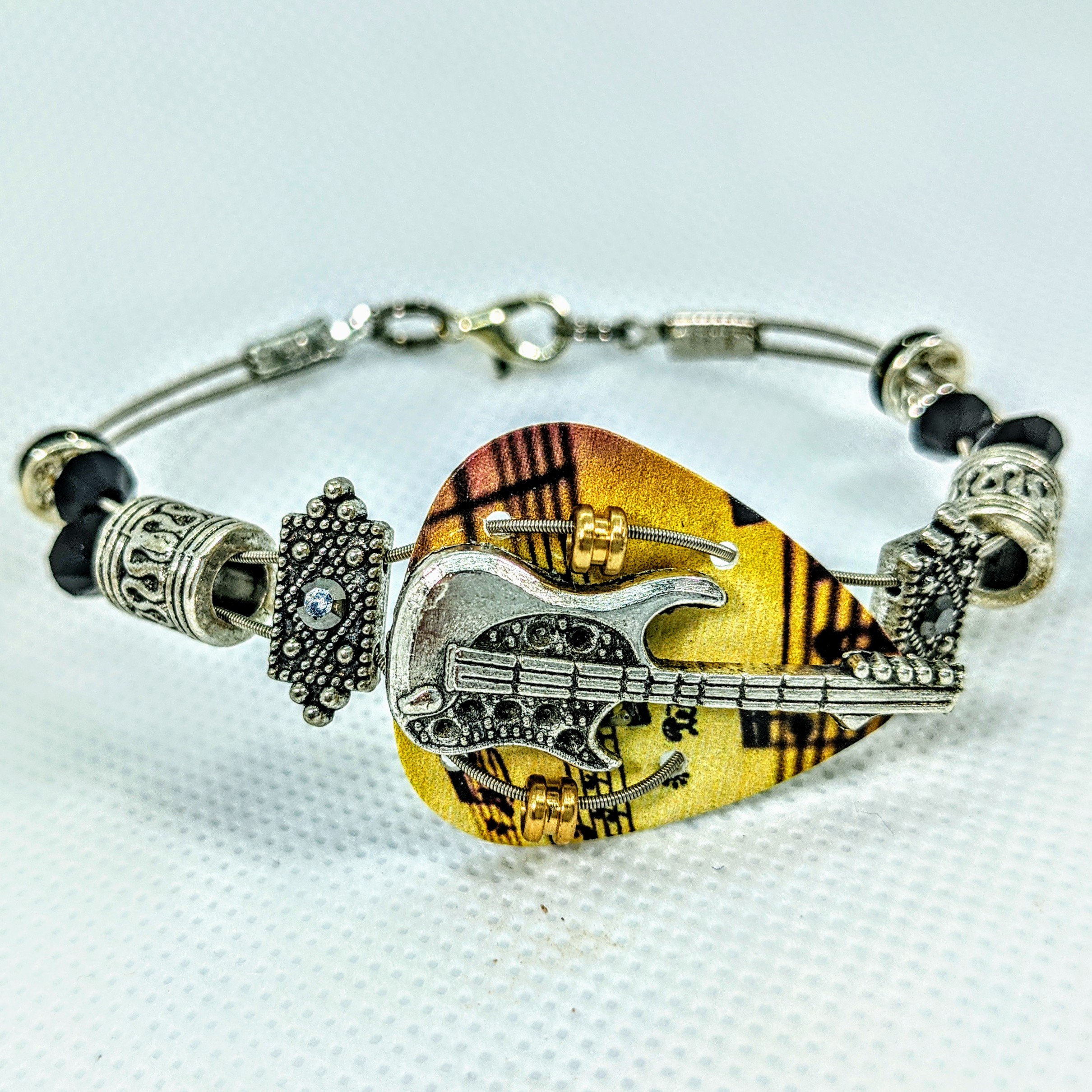 Handmade bracelet made from guitar strings featuring Swarovski™ crystals and a guitar charm, perfect for music lovers.