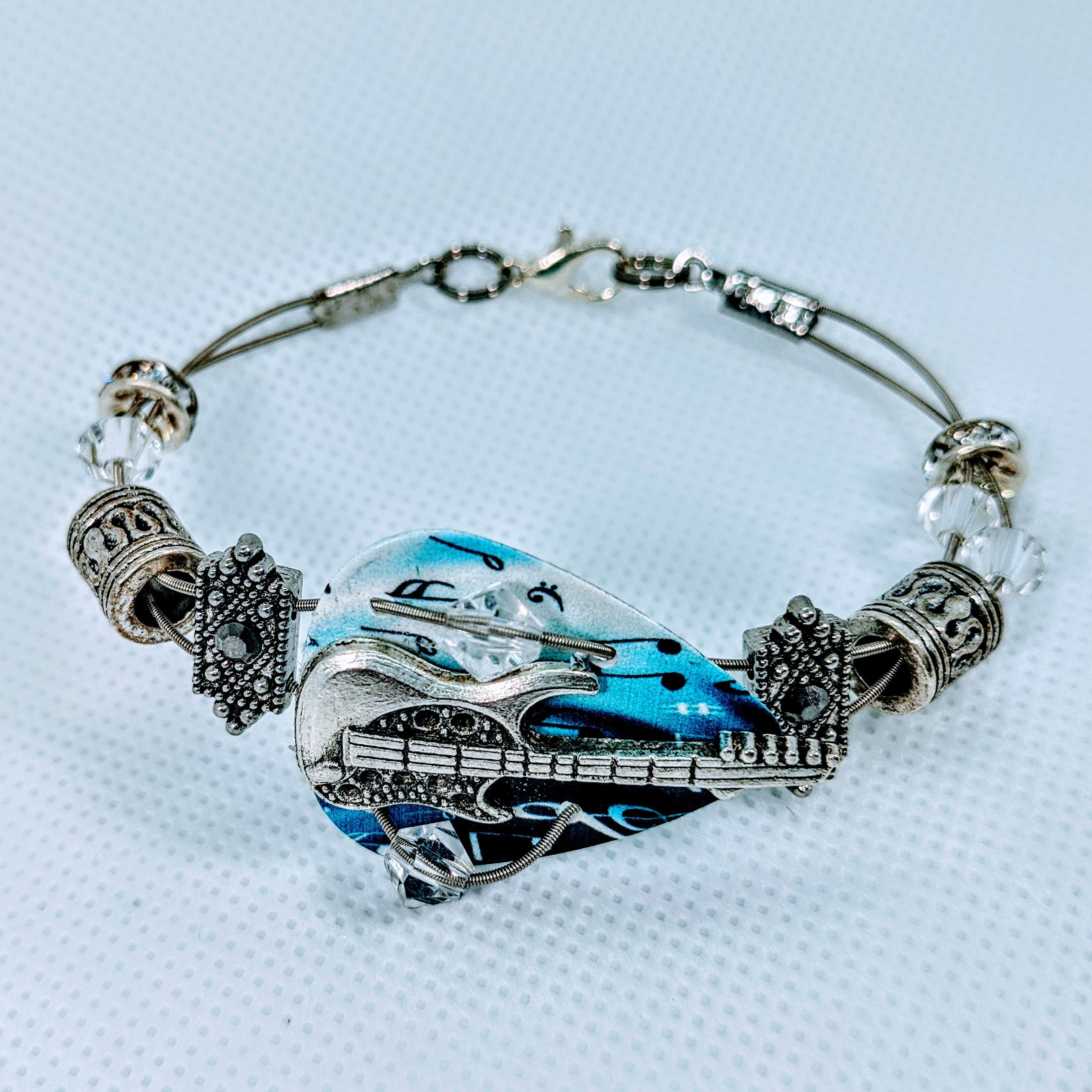 A stylish handmade bracelet made from guitar strings, adorned with sparkling Swarovski™ crystals and a guitar charm, perfect for music lovers.